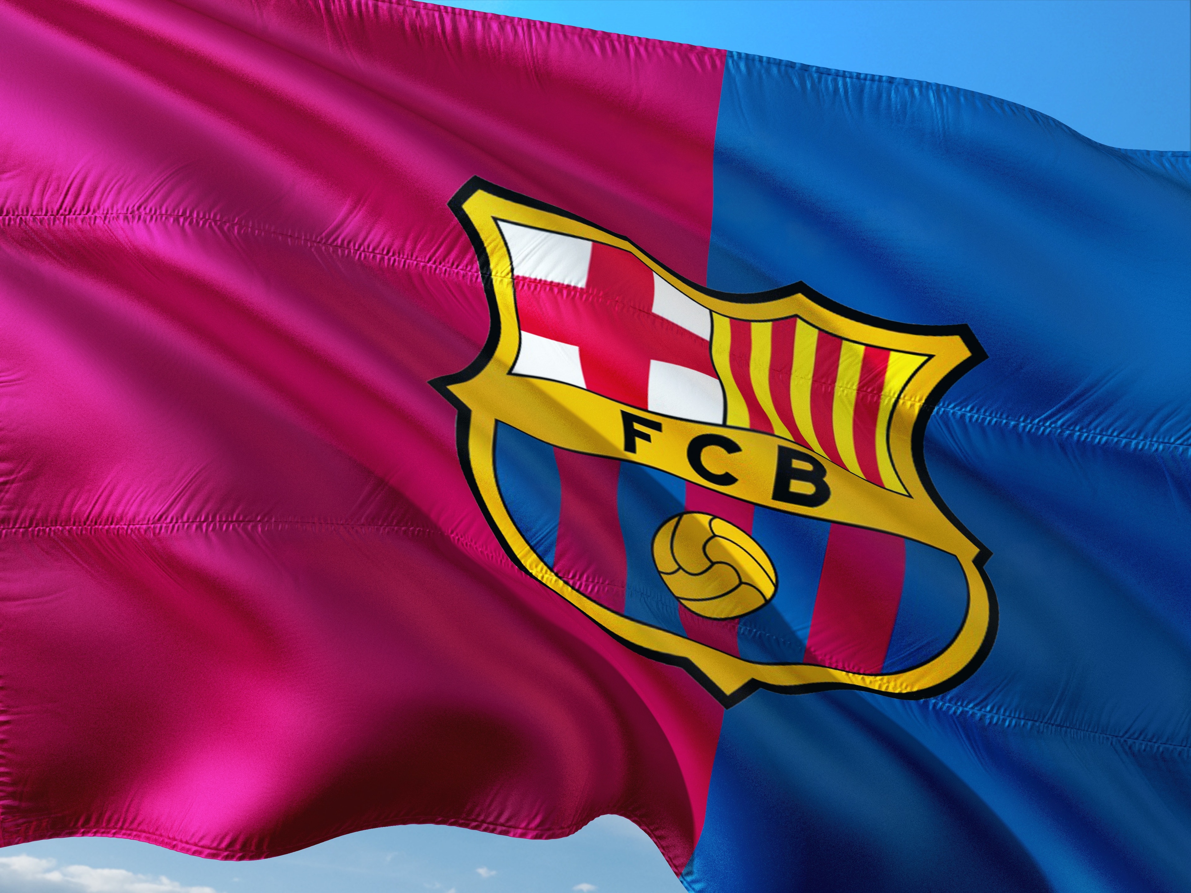 FC Barcelona flagga med klubbens emblem och färger flaxande mot blå himmel. Image by jorono from Pixabay