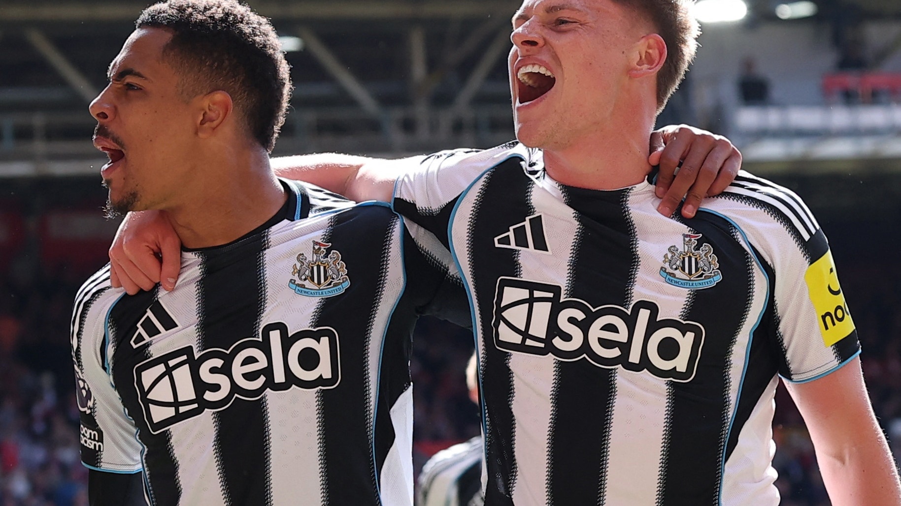 Två fotbollsspelare i Newcastle United-tröjor firar tillsammans på fotbollsplan.
