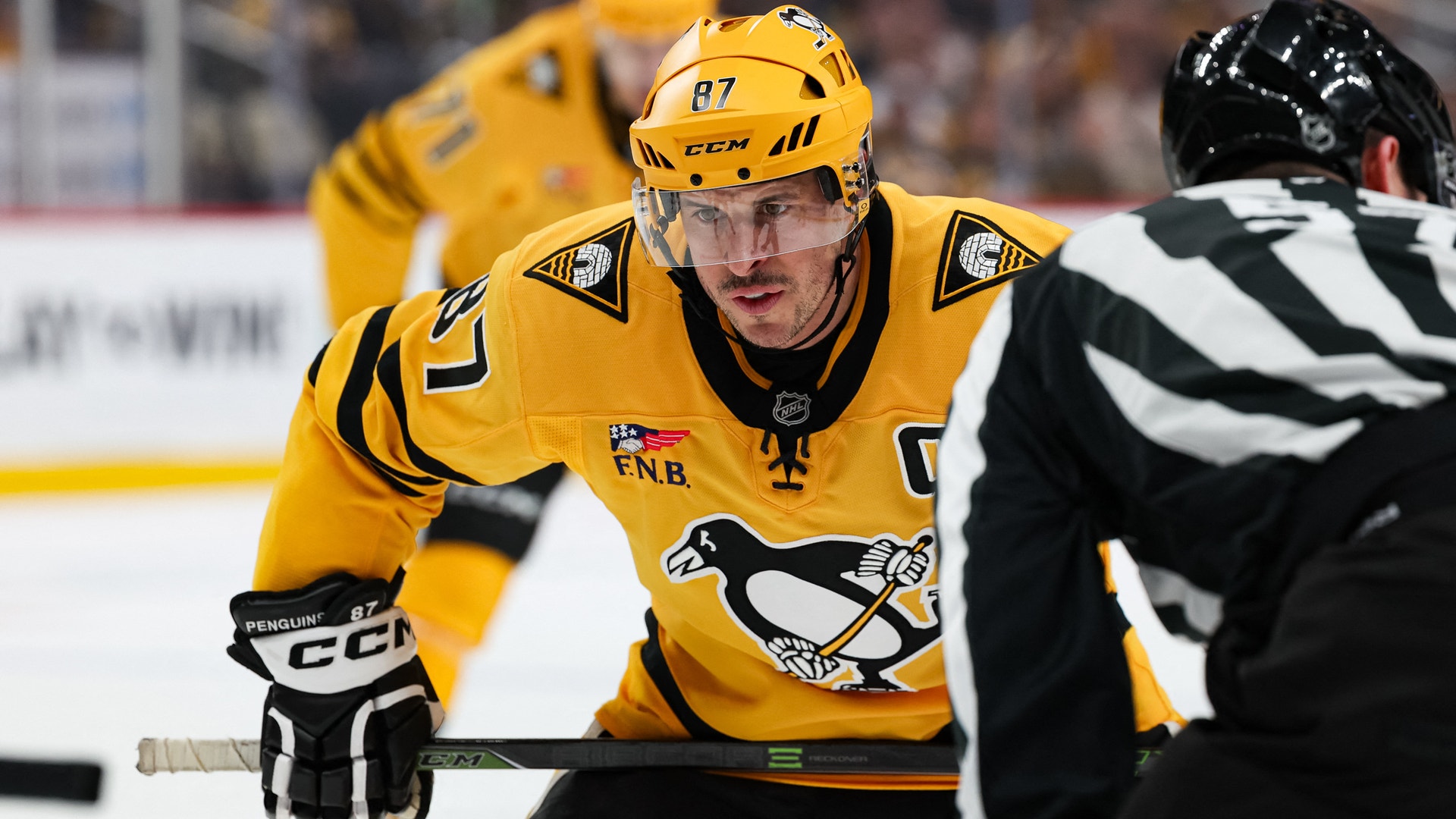 Ishockeyspelare i gul tröja med nummer 87 under en match, med motspelare i svart tröja bredvid sig.