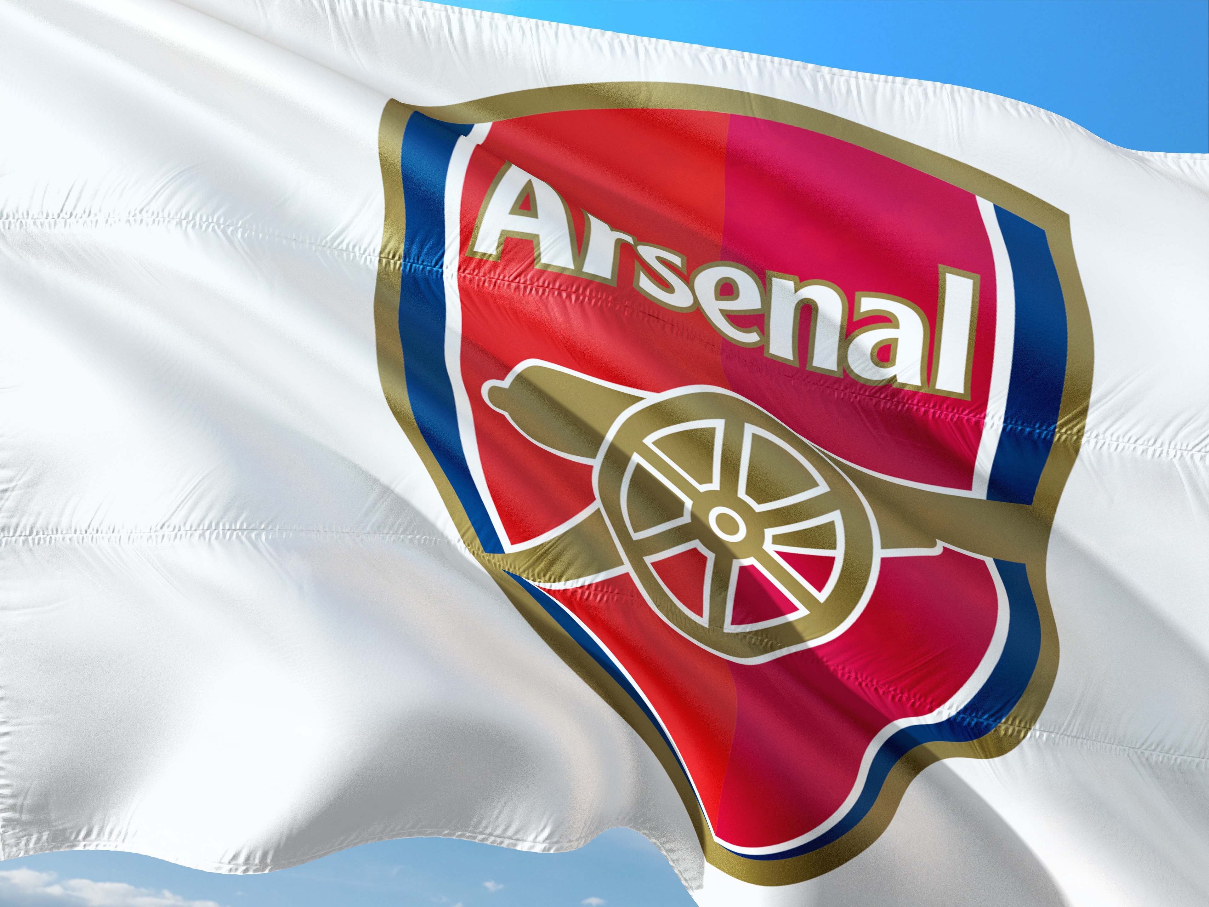 Arsenals fotbollsklubbemblem på en vit flagga som vajar mot blå himmelImage by jorono from Pixabay

 