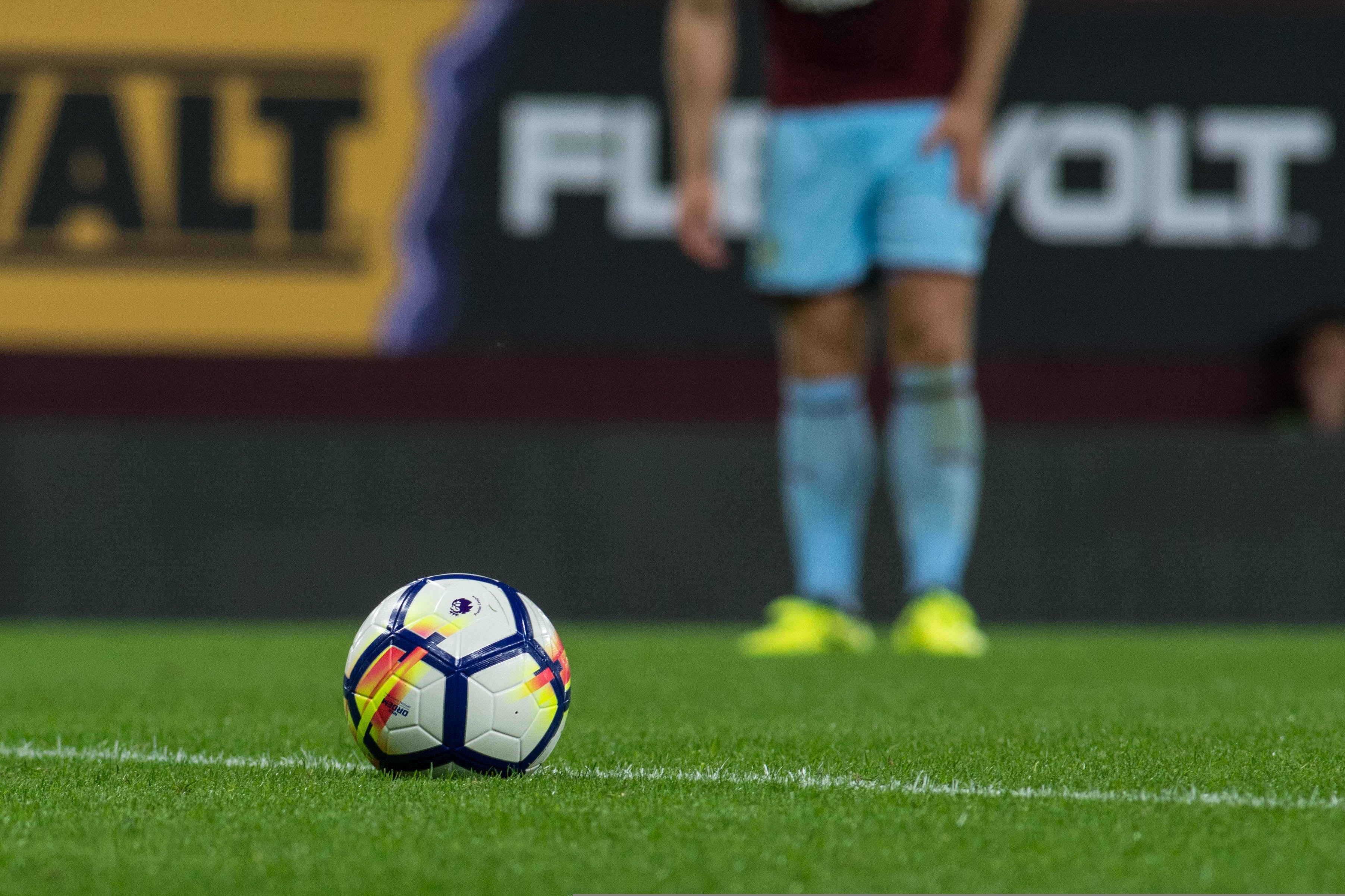 En fotboll på en gräsplan med en spelare i bakgrunden. Image by Kelvin Stuttard from Pixabay