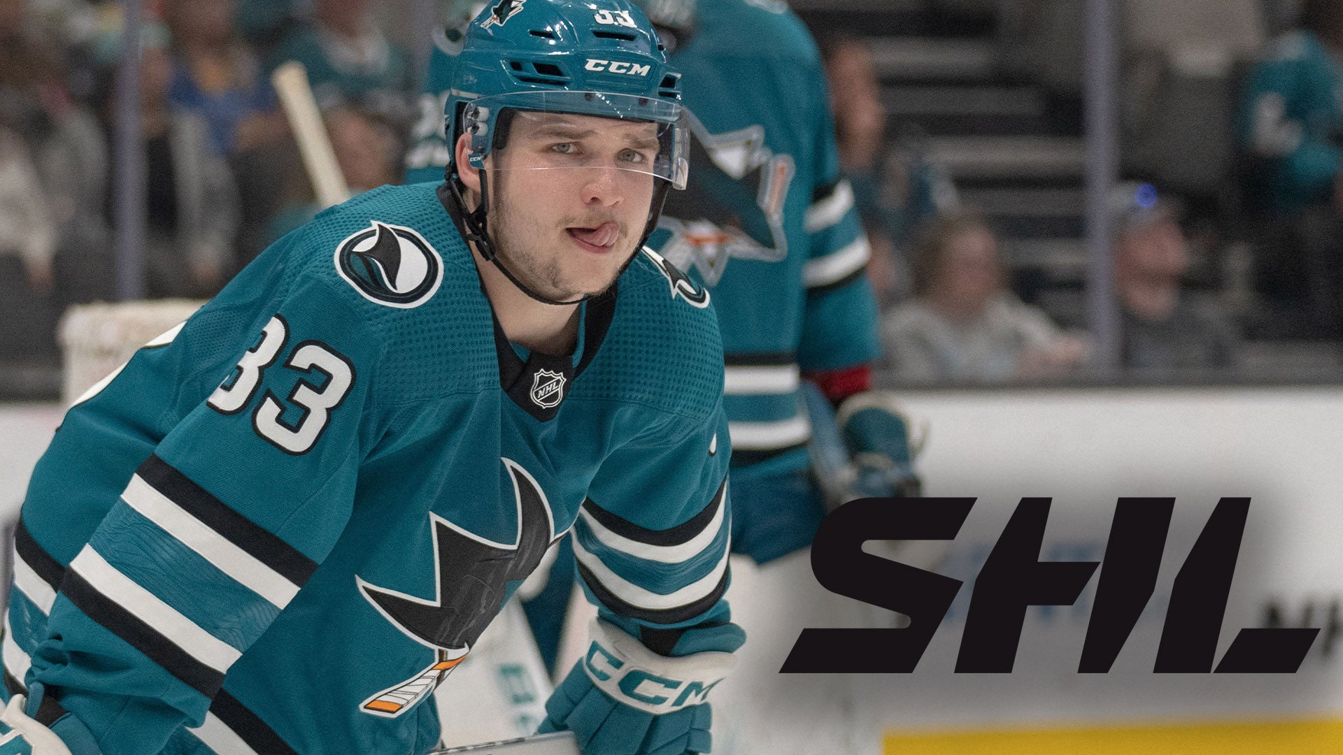 Ishockeyspelare i teal-blå uniform med nummer 33 under en match. Spelaren är i rörelse på isen med fokuserad blick.