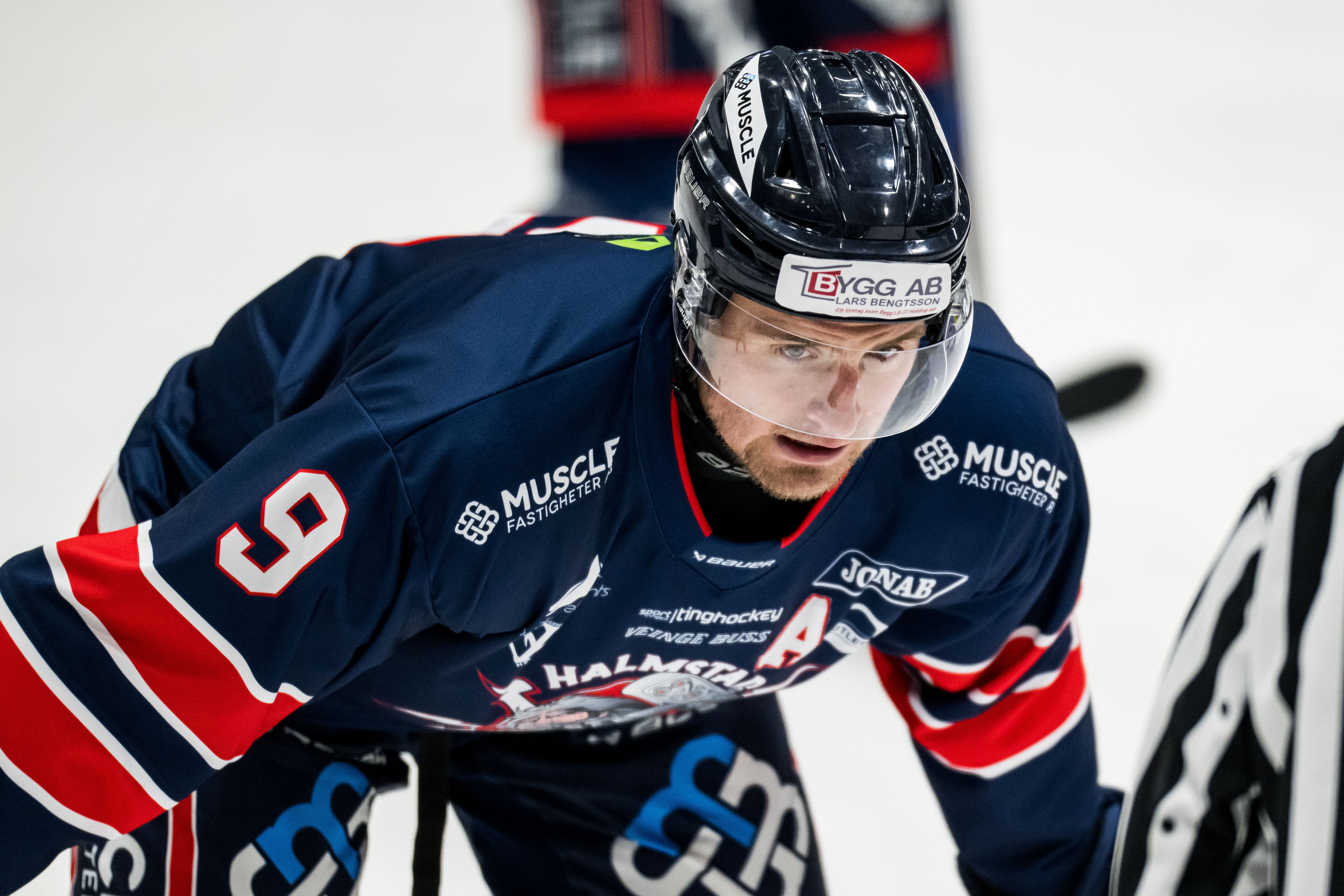 Ishockeyspelare i mörkblå tröja med nummer 5 under en match. Spelaren bär hjälm och är fokuserad på spelet.