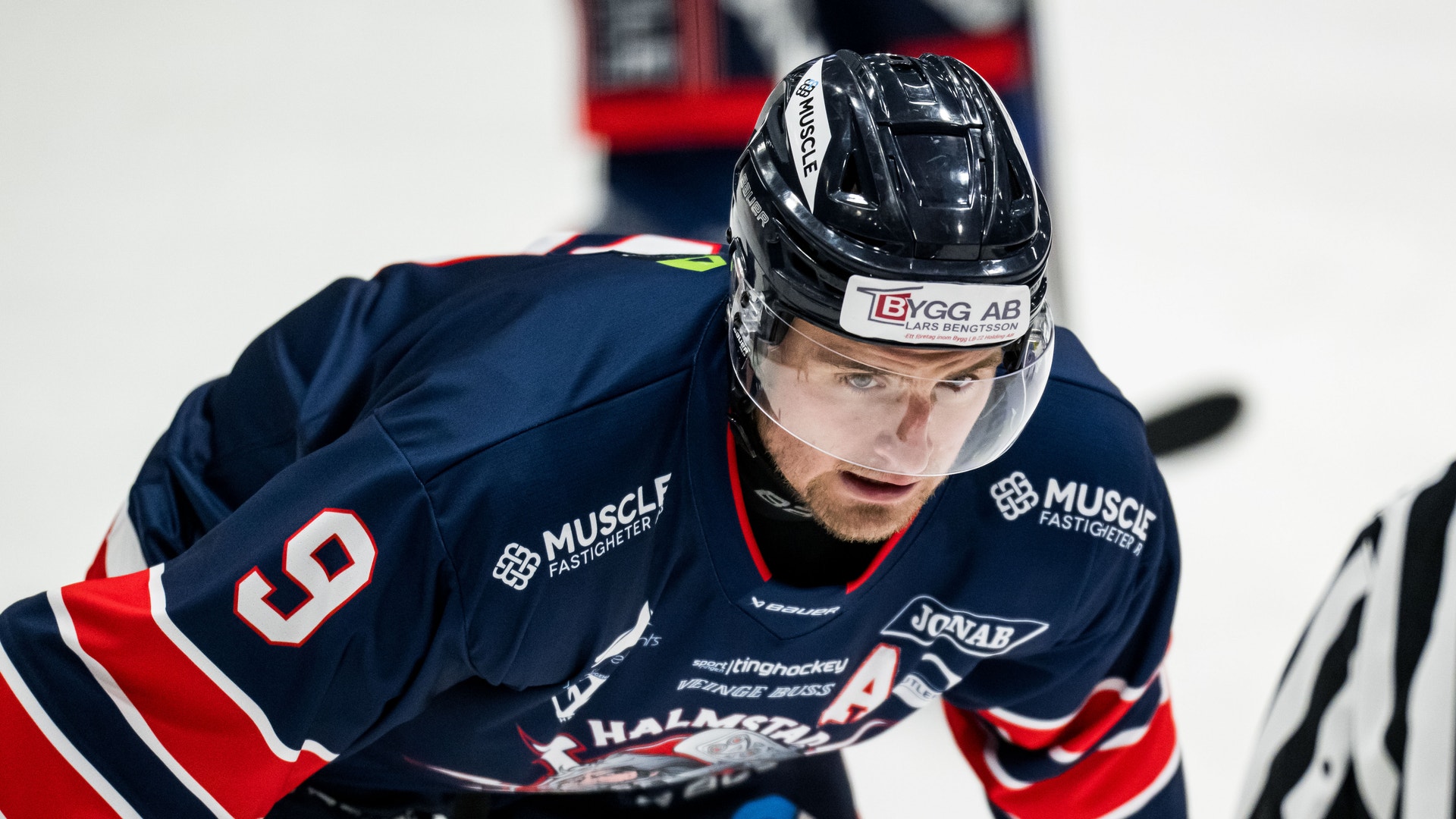 Ishockeyspelare i mörkblå tröja med nummer 5 under en match. Spelaren bär hjälm och är fokuserad på spelet.