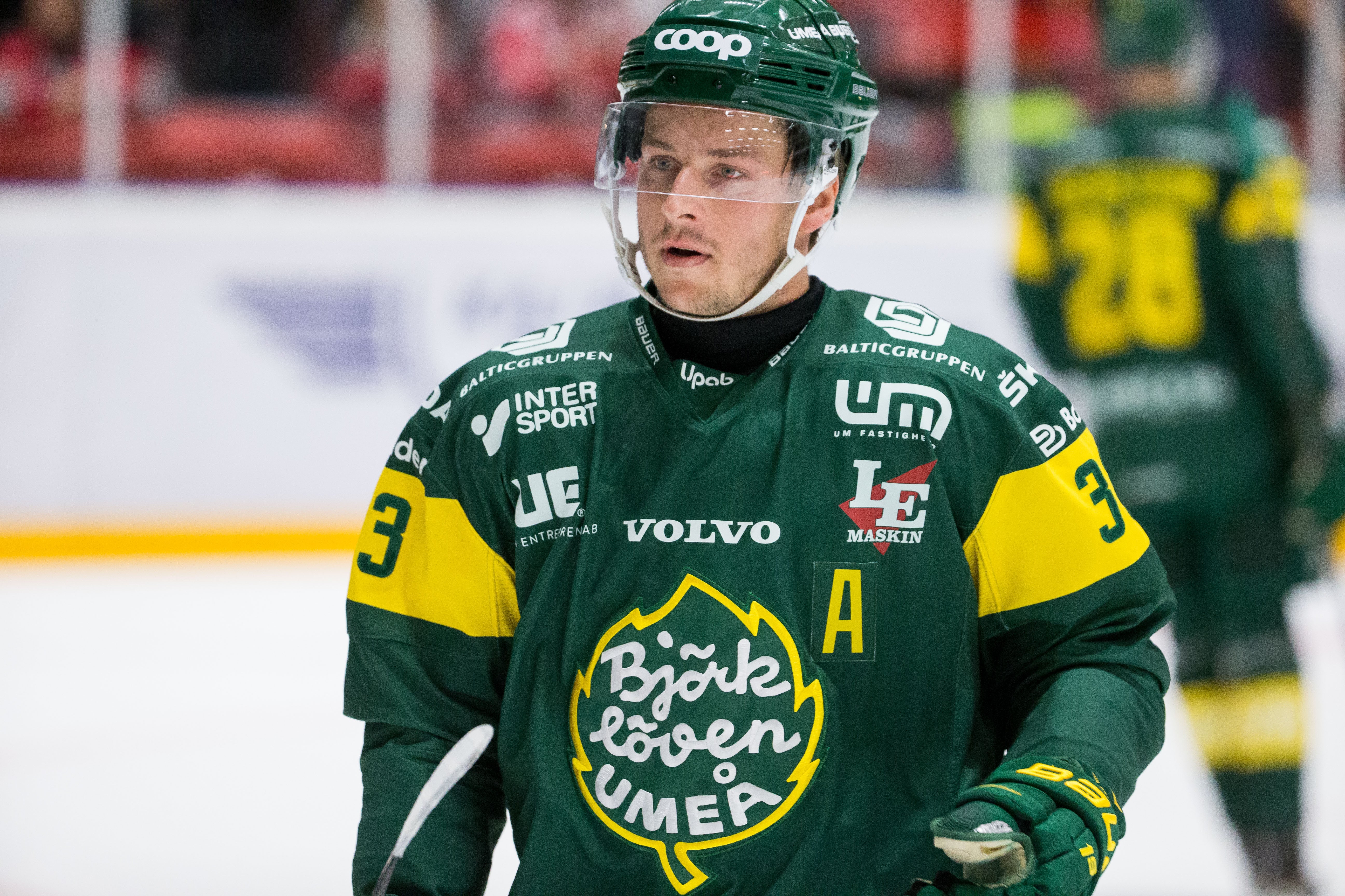 Ishockeyspelare i grön och gul matchdräkt med hjälm under en ishockeymatch.