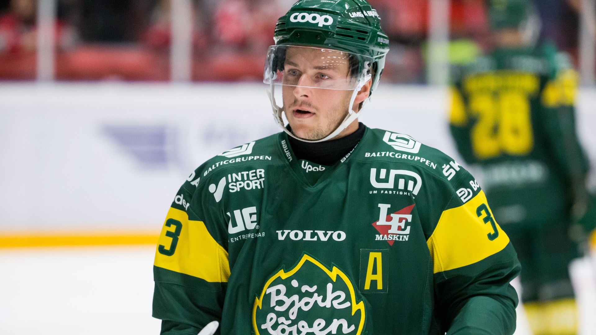 Ishockeyspelare i grön och gul matchdräkt med hjälm under en ishockeymatch.