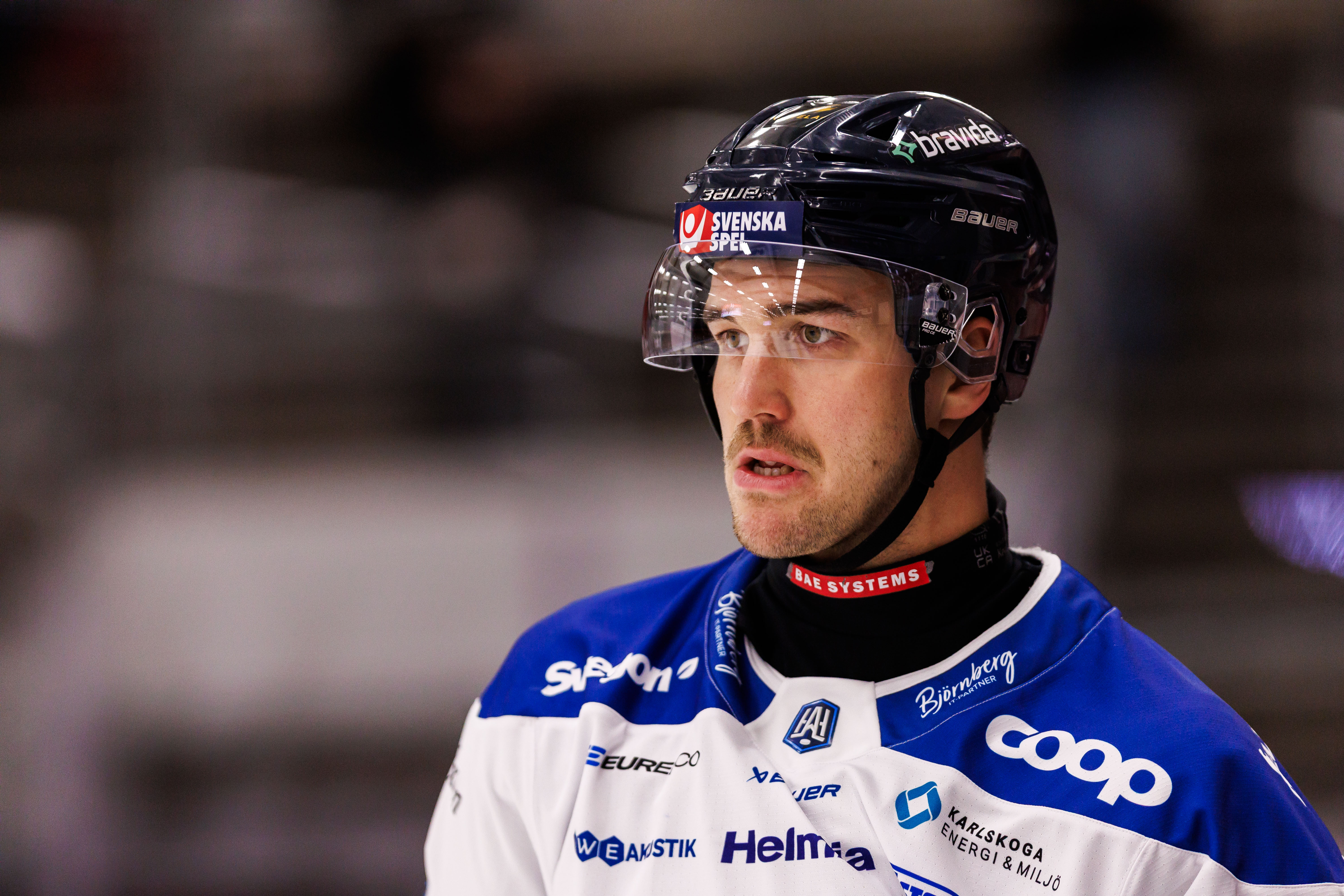 Porträtt av en ishockeyspelare i blå och vit matchdräkt med svart hjälm under en match.
