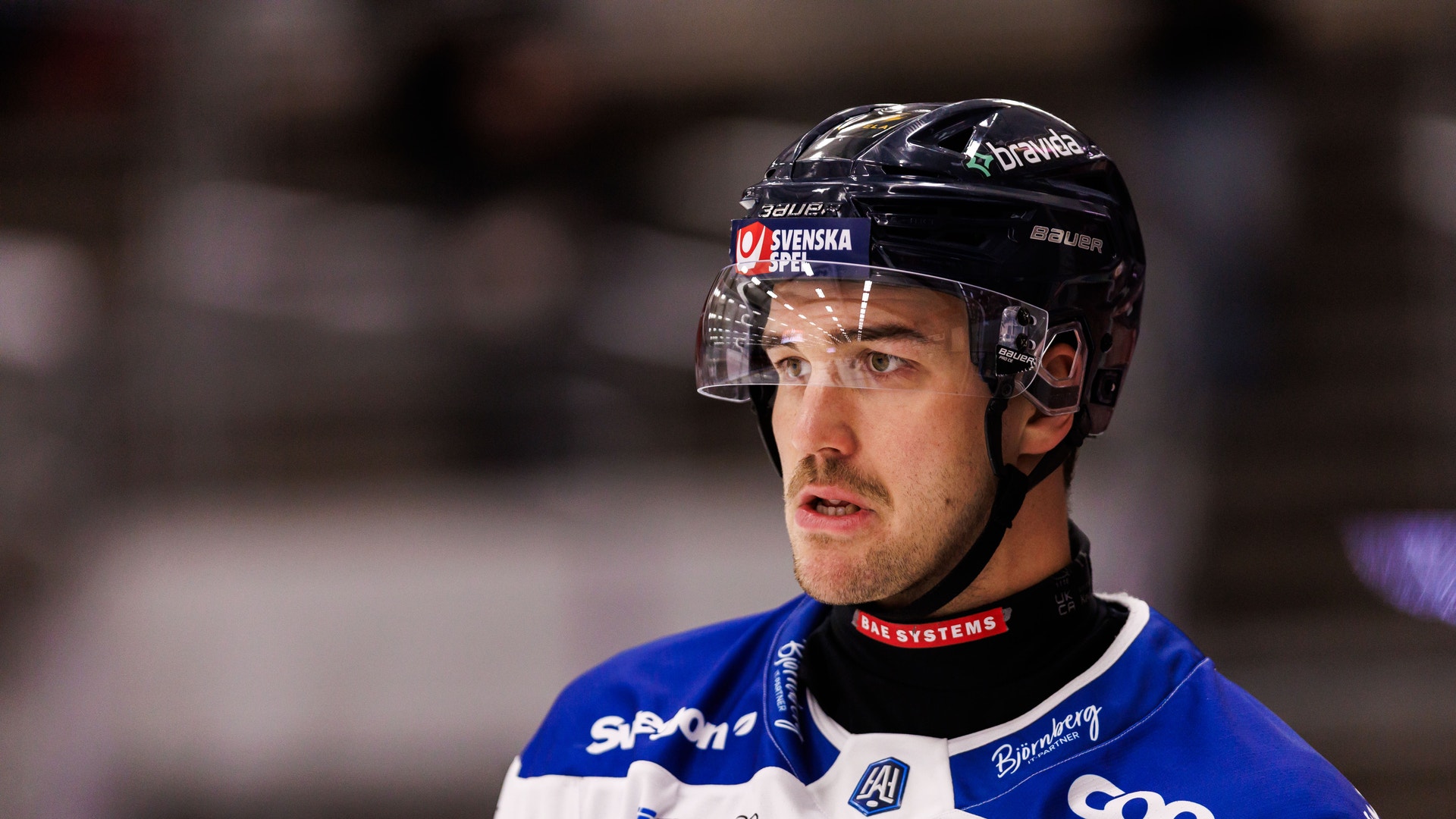 Porträtt av en ishockeyspelare i blå och vit matchdräkt med svart hjälm under en match.