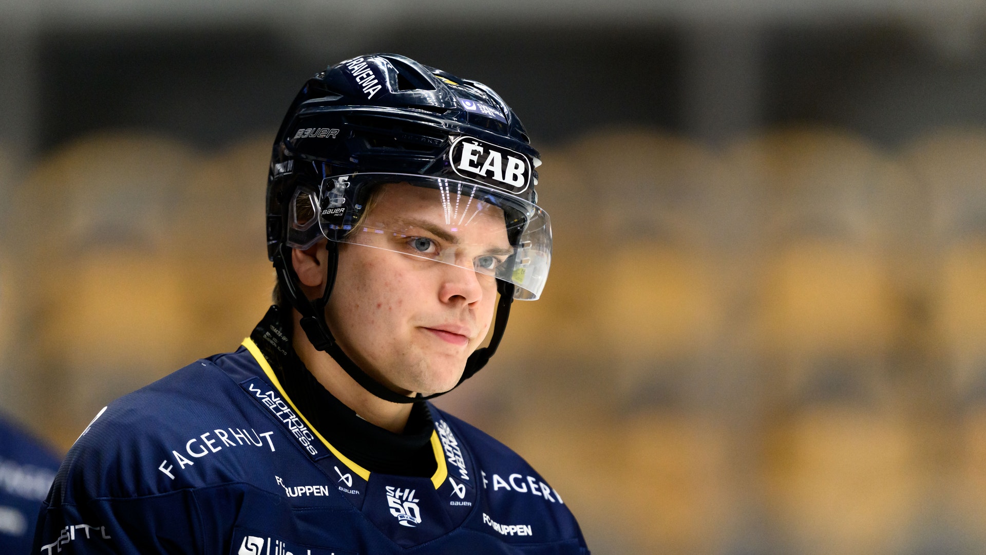 Ishockeyspelare i mörkblå tröja med gula detaljer och svart hjälm under en match.