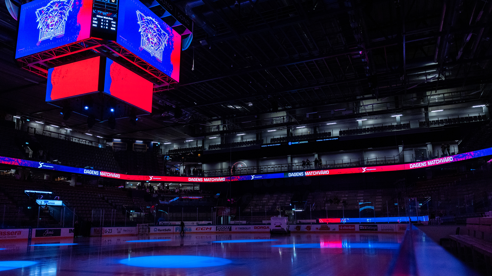 En tom ishockeyhall med blå och röd scenbelysning. Isen är reflekterande och ljuset skapar en dramatisk atmosfär i arenan.