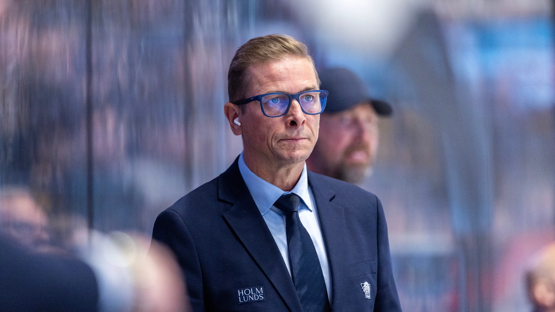 Man i mörk kostym och glasögon vid ishockeytillfälle