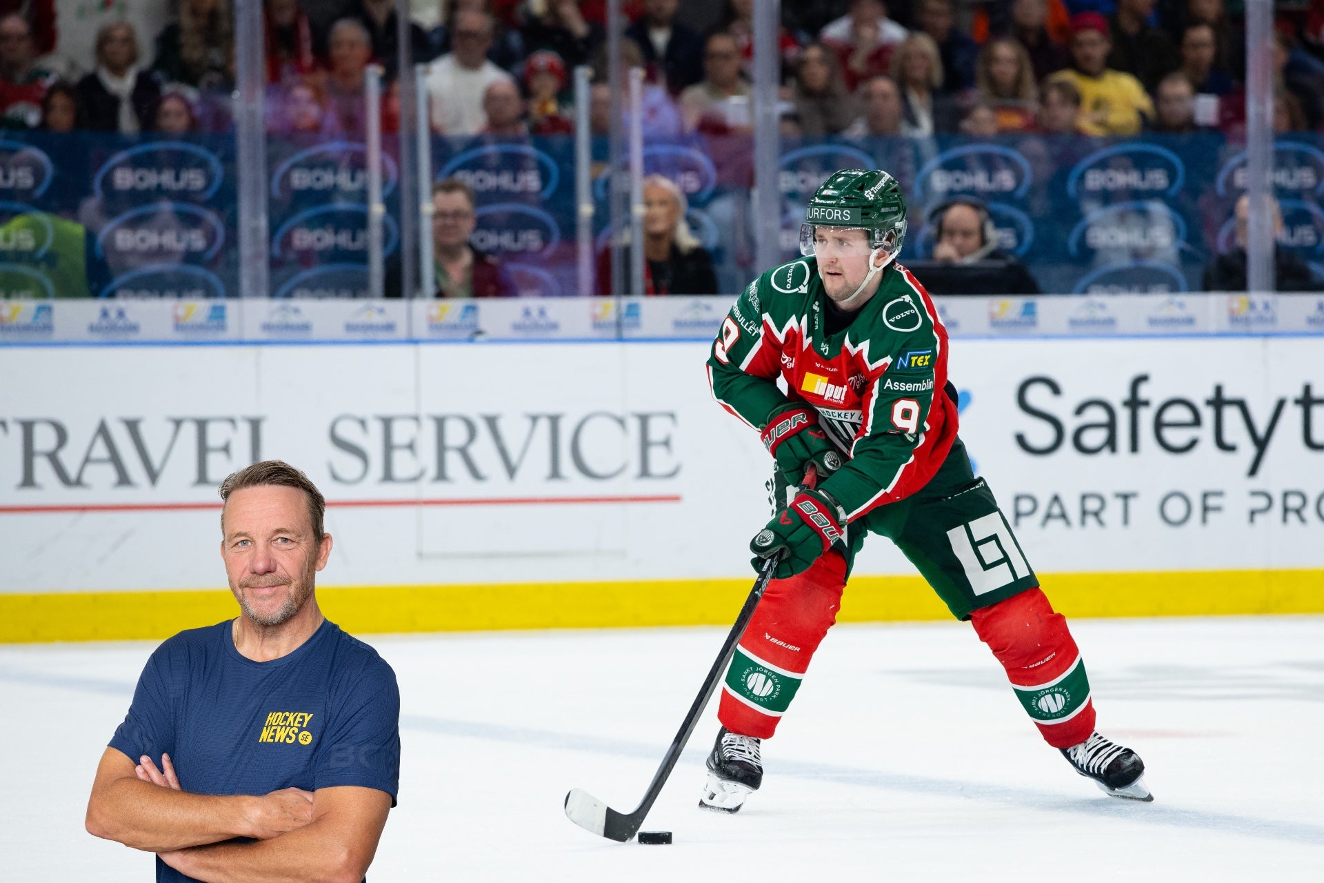 Ishockeyspelare i röd och grön tröja spelar på isen med hockey stick och puck. En man i blå t-shirt står i förgrunden. Publik syns i bakgrunden.