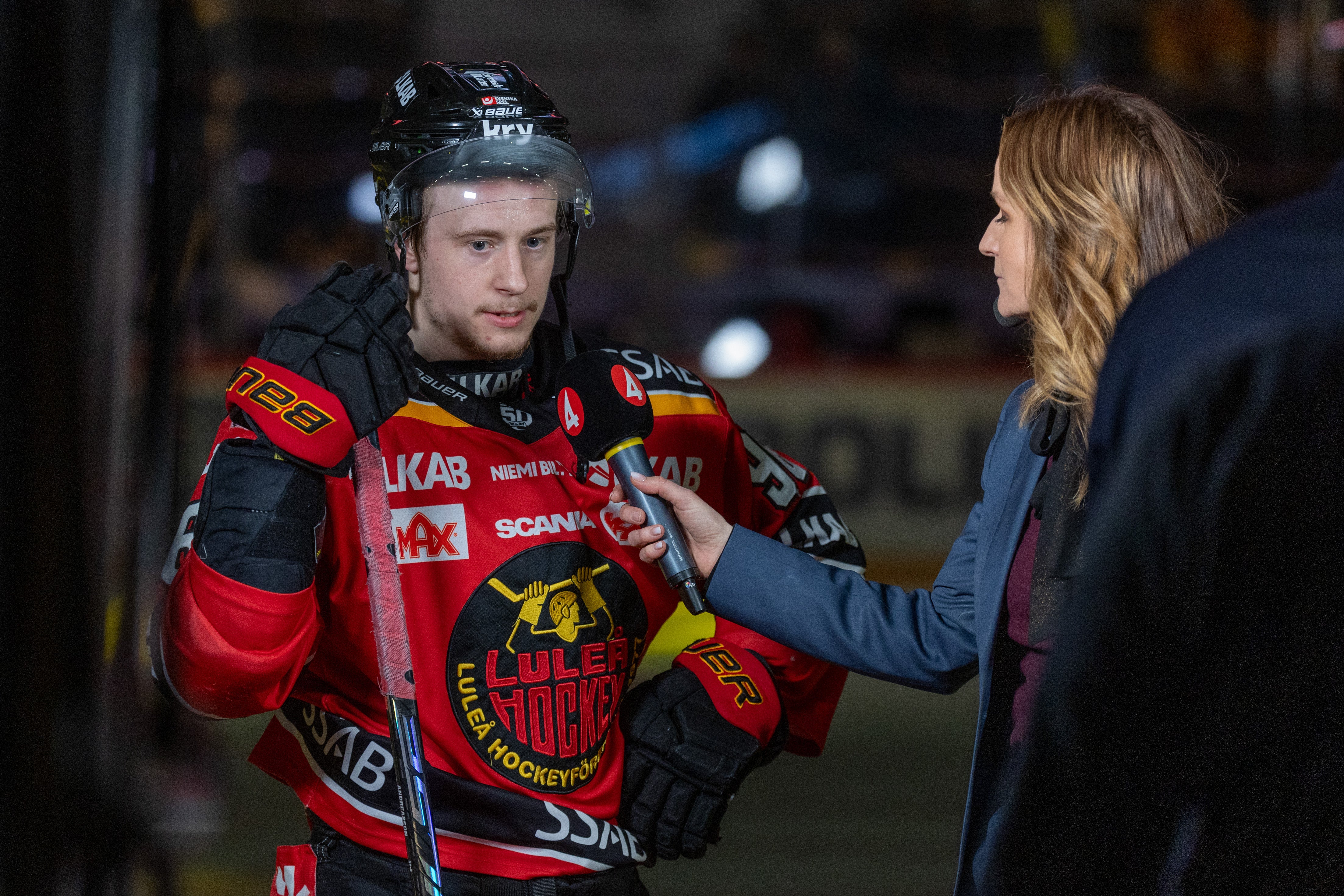 En ishockeyspelare i röd och svart tröja blir intervjuad av en reporter.