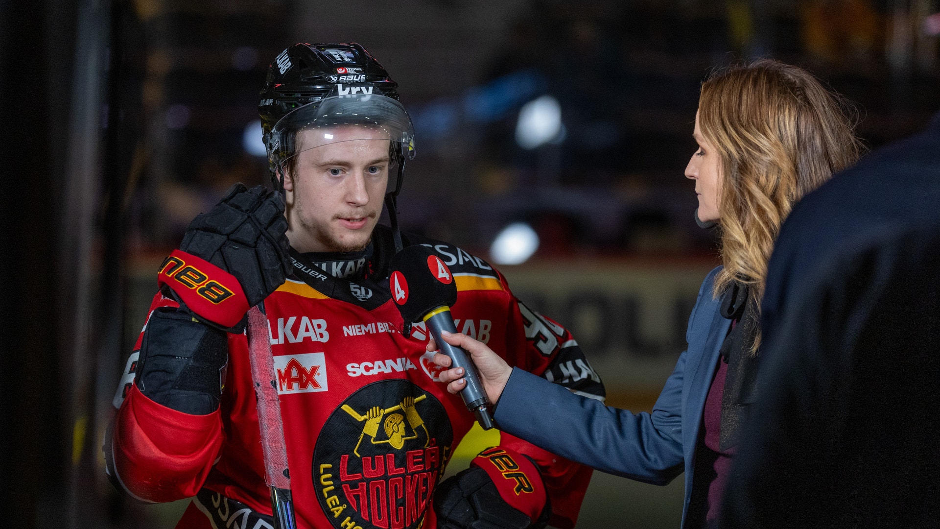 En ishockeyspelare i röd och svart tröja blir intervjuad av en reporter.