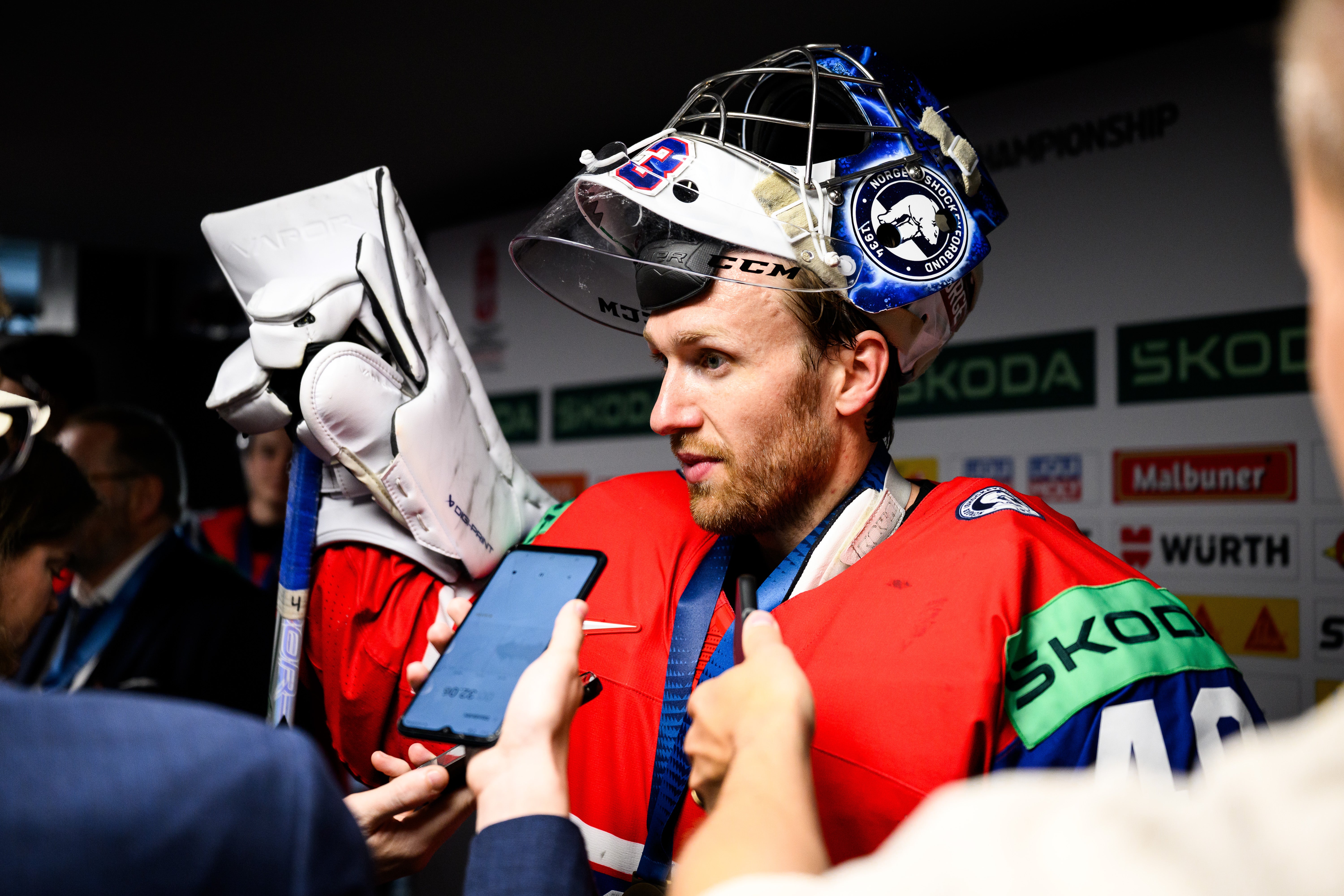 Ishockeyspelare i röd tröja med guldmedalj håller en vinnartrofé efter en framgångsrik match.