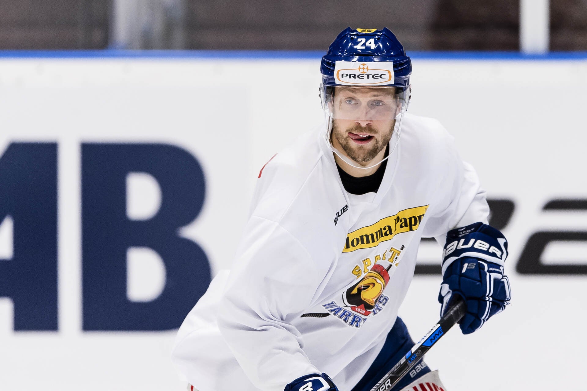 Ishockeyspelare i vit tröja med nummer 24 i rörelse på isen med hjälm och ishockeyklubb.