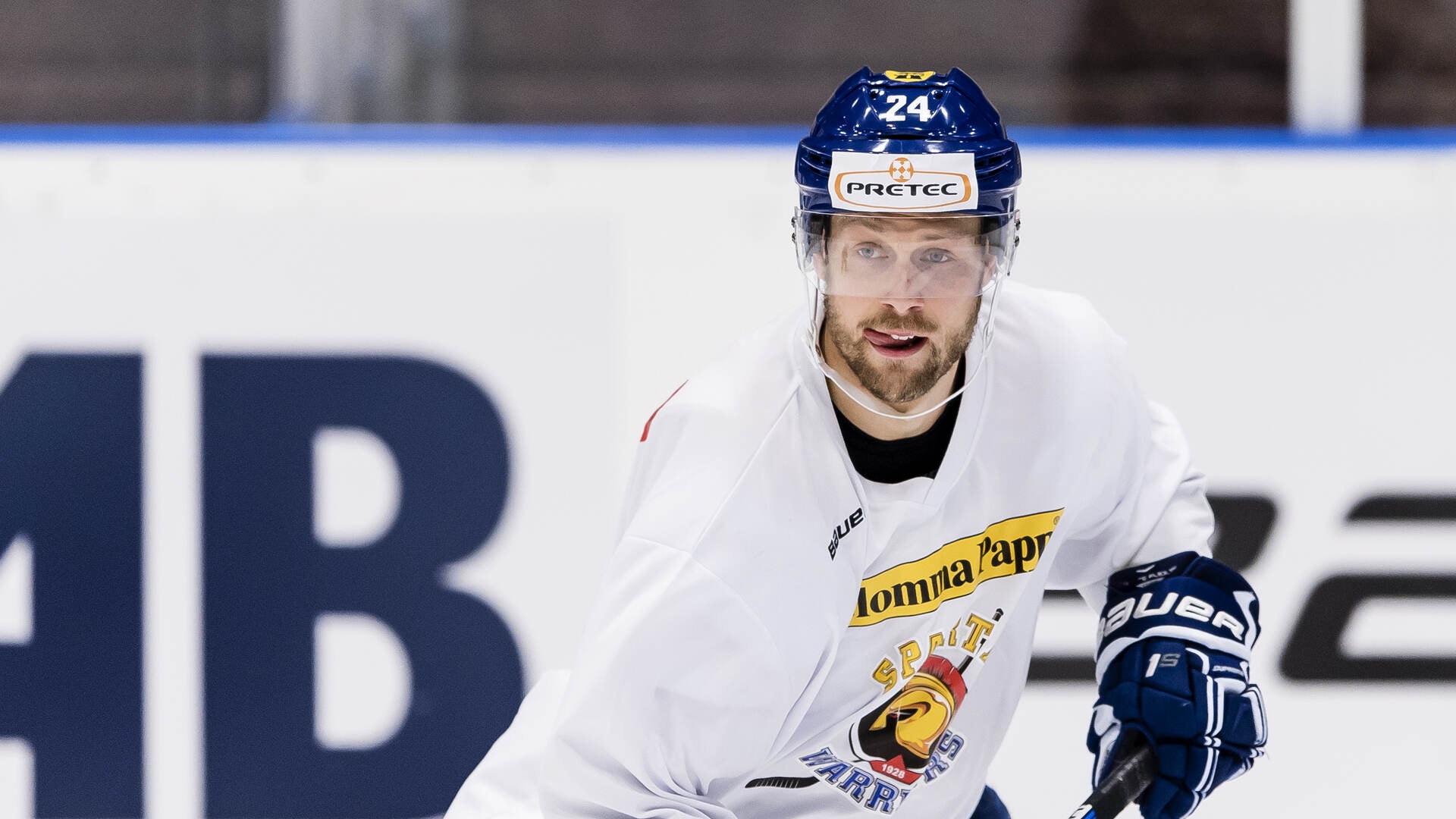 Ishockeyspelare i vit tröja med nummer 24 i rörelse på isen med hjälm och ishockeyklubb.