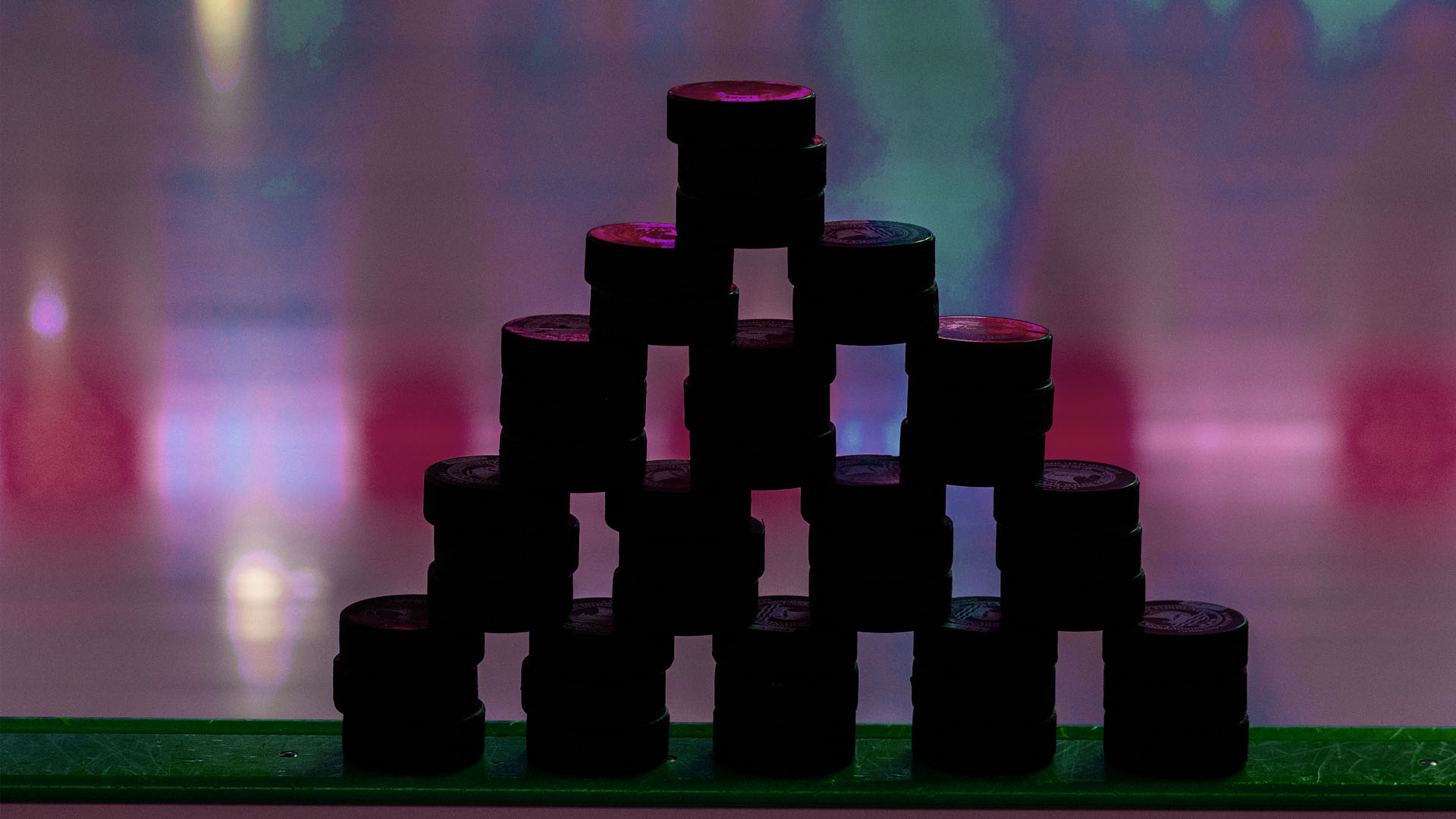 En pyramid av svarta cylindrar mot en färgglad bakgrund med rosa, lila och blå ljus.