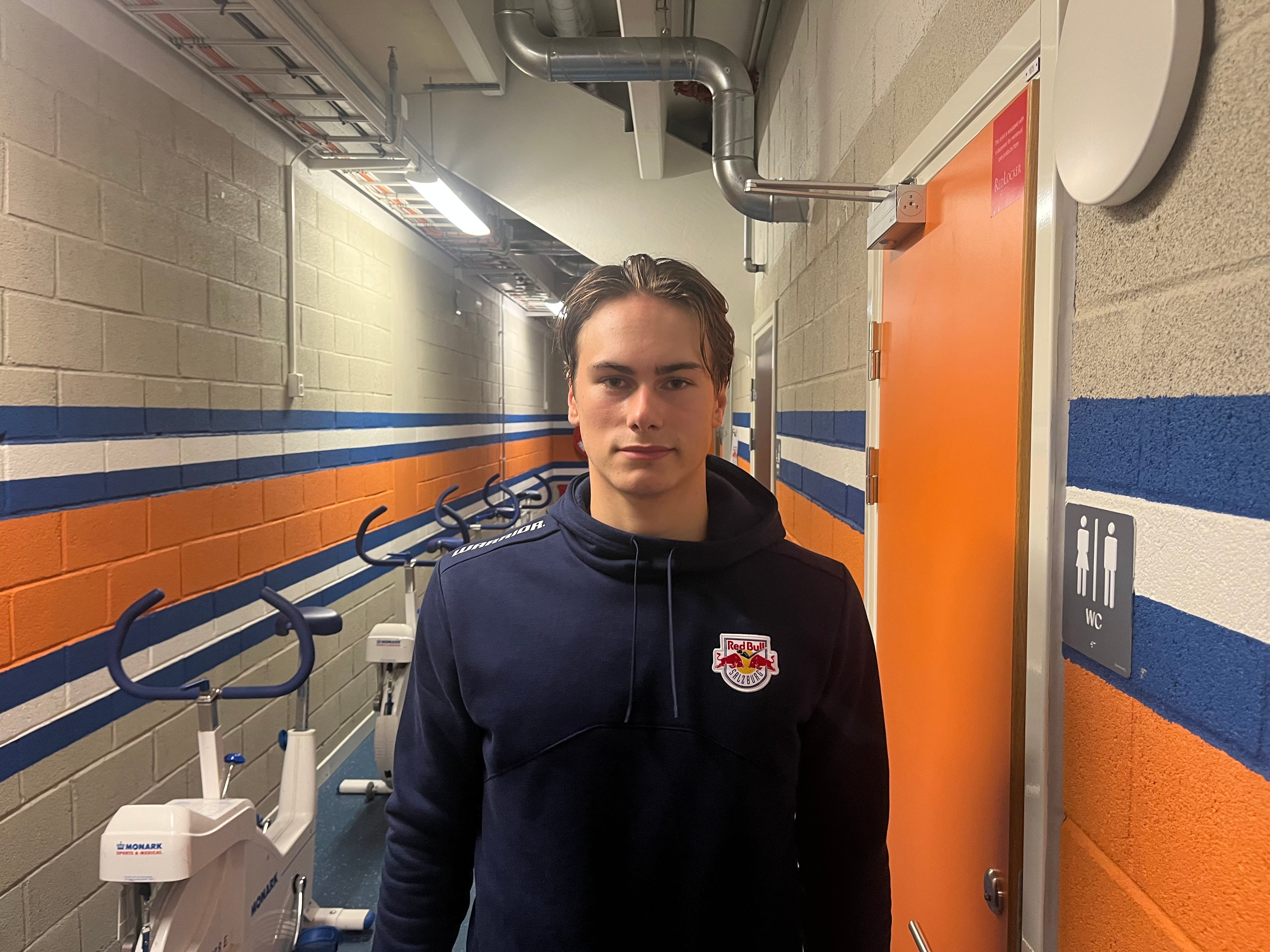En ung man i mörkblå huvtröja med Red Bull-logga står i en korridor med blå och orange väggmålning.