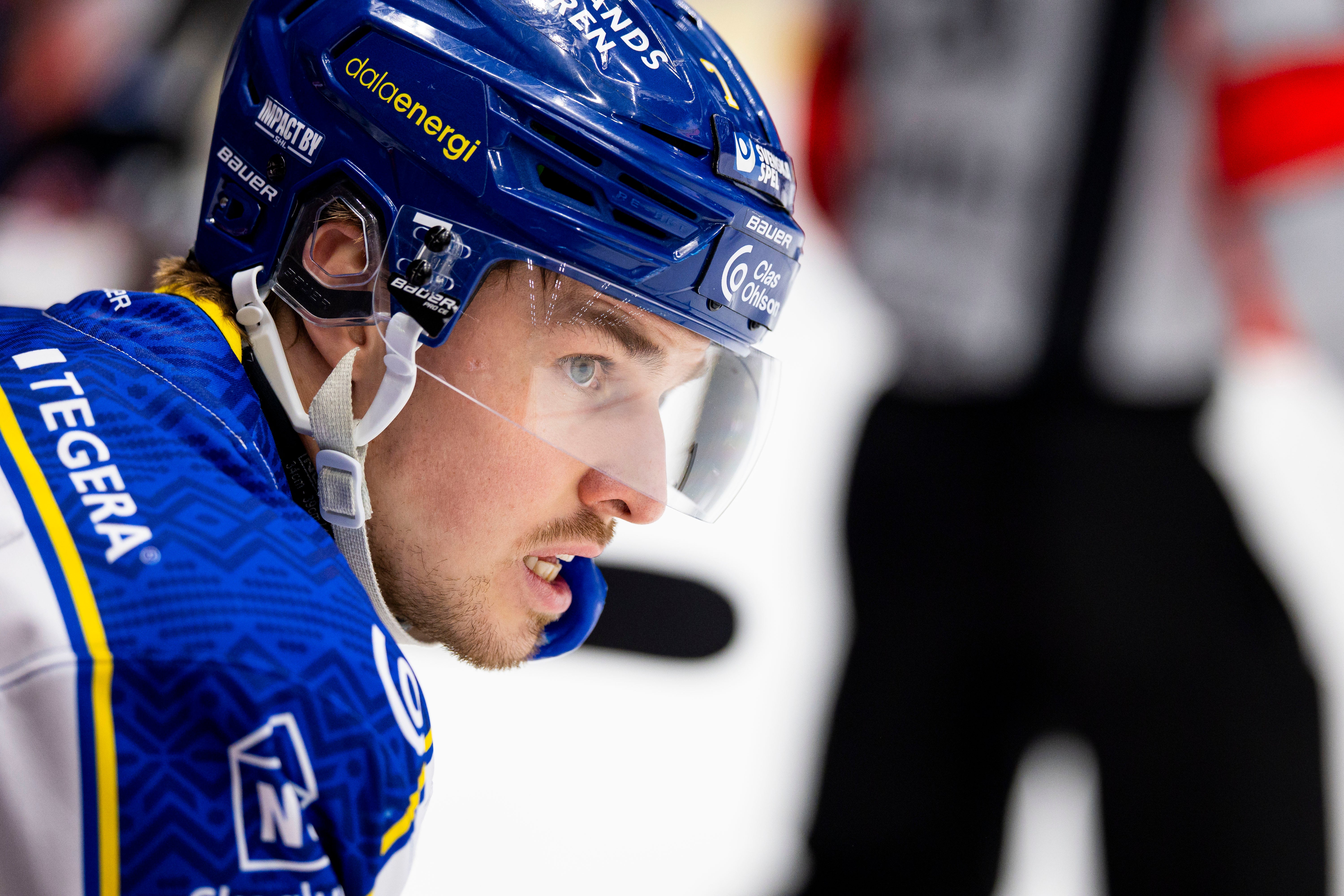 Porträttbild av en ishockeyspelare i blå uniform och hjälm under en match.