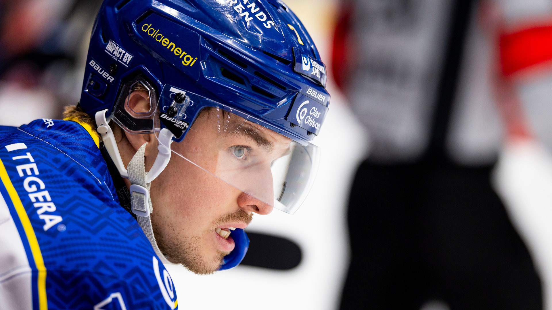 Porträttbild av en ishockeyspelare i blå uniform och hjälm under en match.