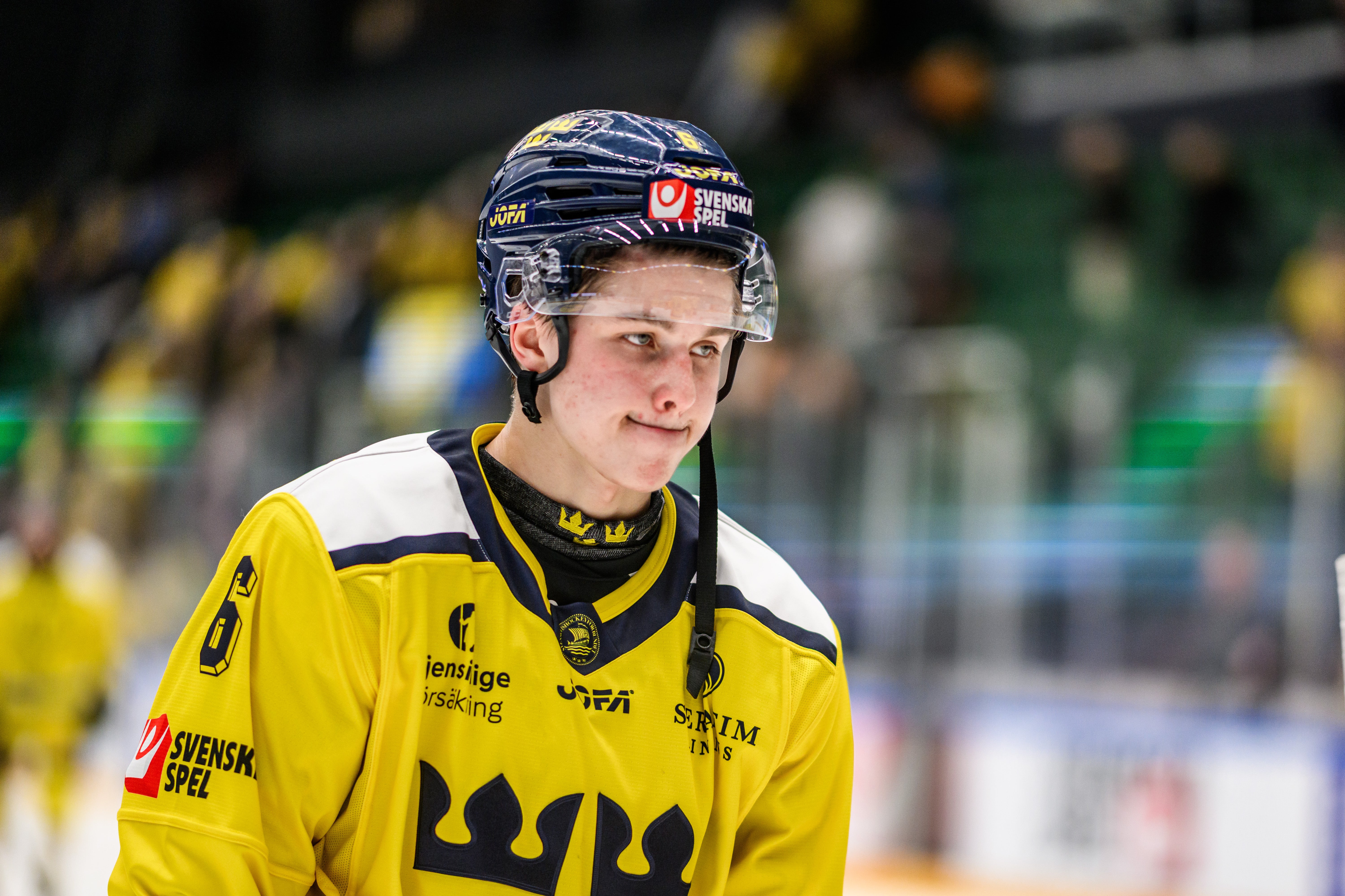 Ishockeyspelare i gul och blå landslagströja med hjälm under en match.