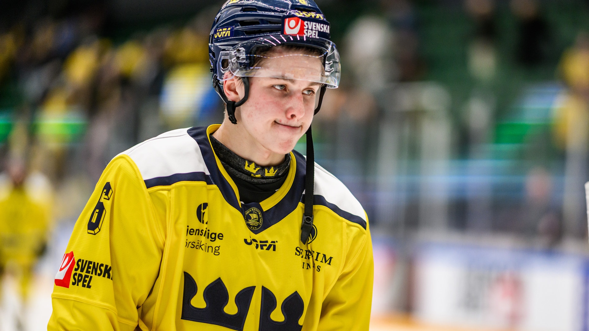 Ishockeyspelare i gul och blå landslagströja med hjälm under en match.