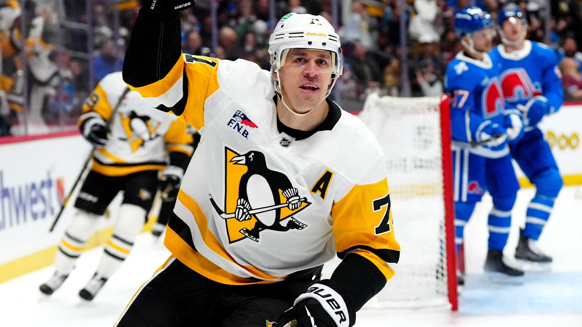Ishockeyspelare i Pittsburgh Penguins vita och gula tröja under en match. Spelaren är i aktion på isen med motsatta lag synliga i bakgrunden.