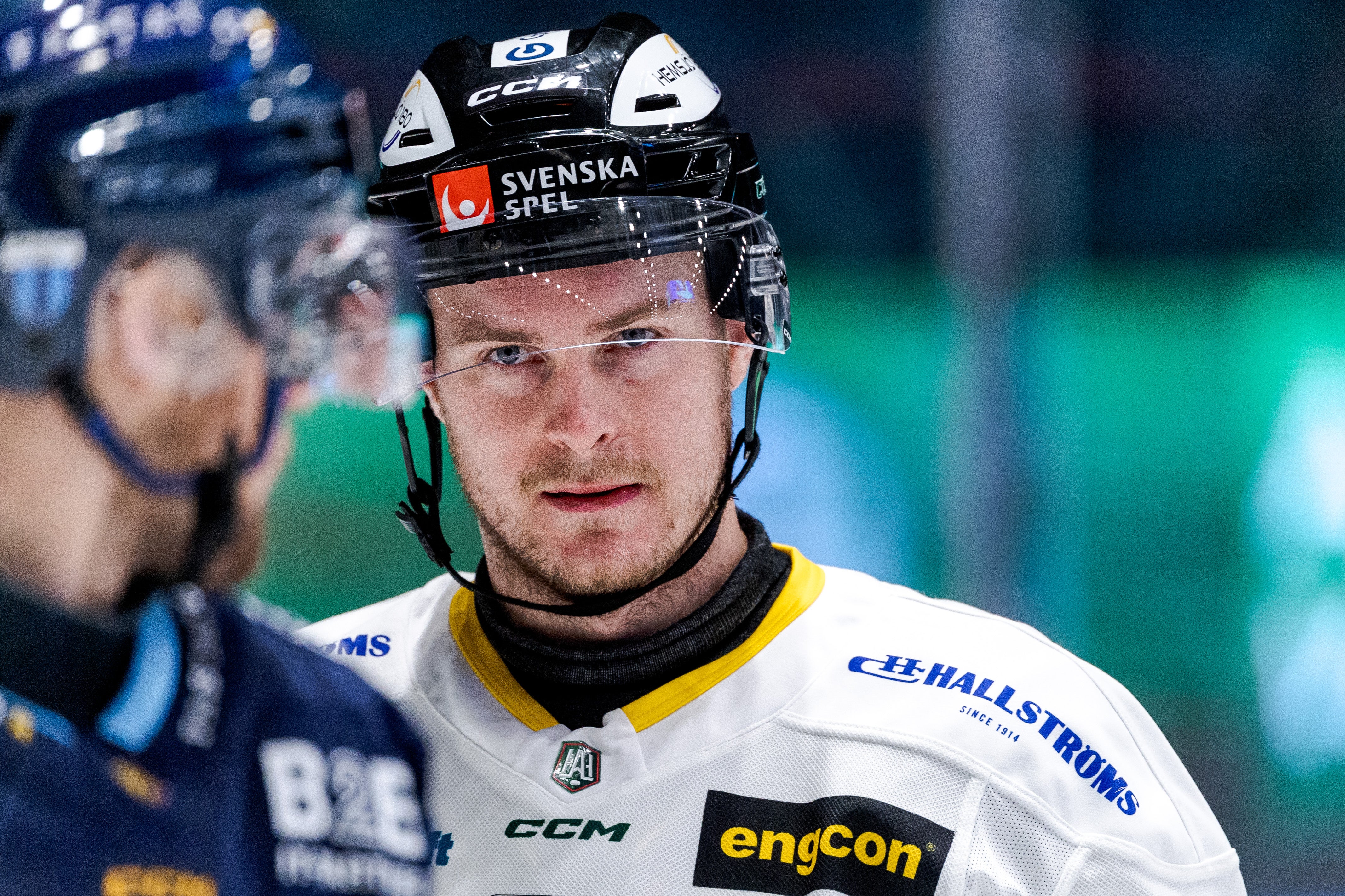 Ishockeyspelare i vit tröja med hjälm märkt Svenska Spel, fotograferad under en match.