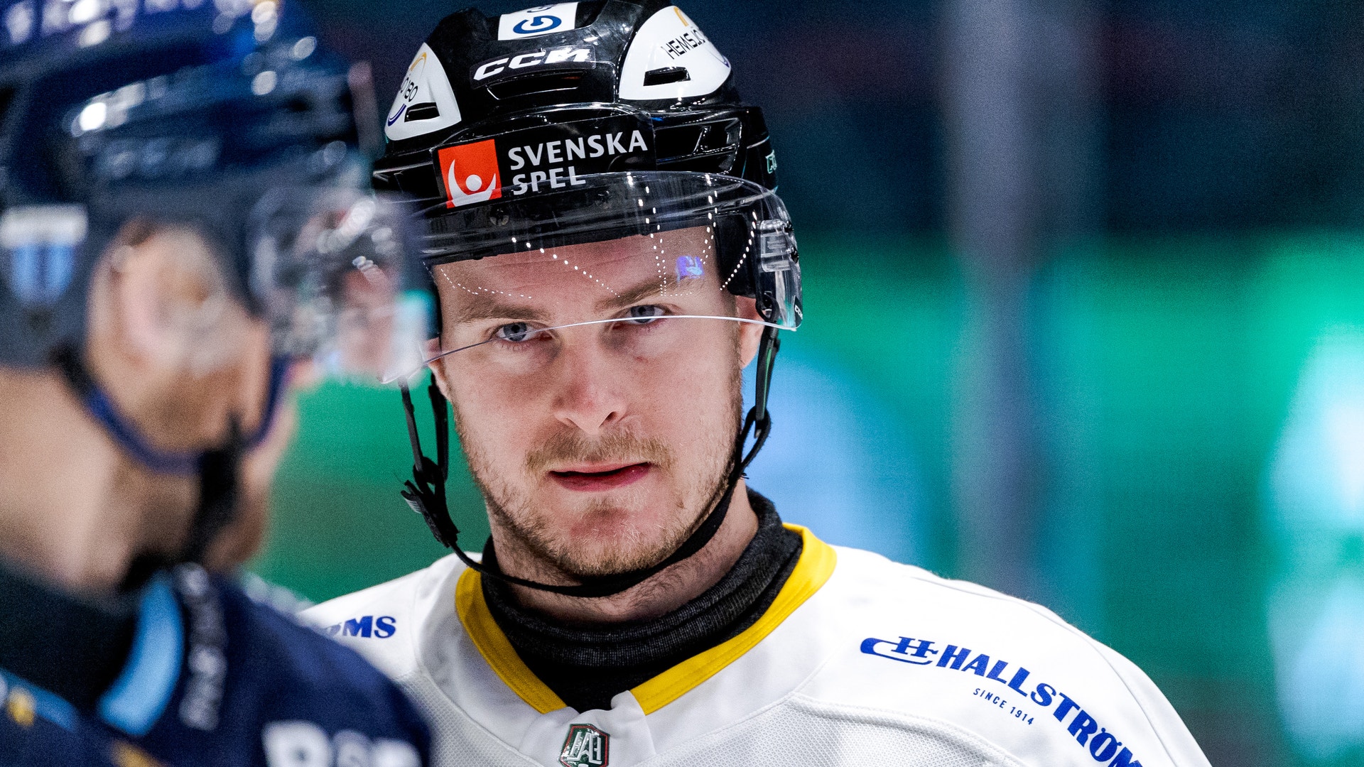 Ishockeyspelare i vit tröja med hjälm märkt Svenska Spel, fotograferad under en match.