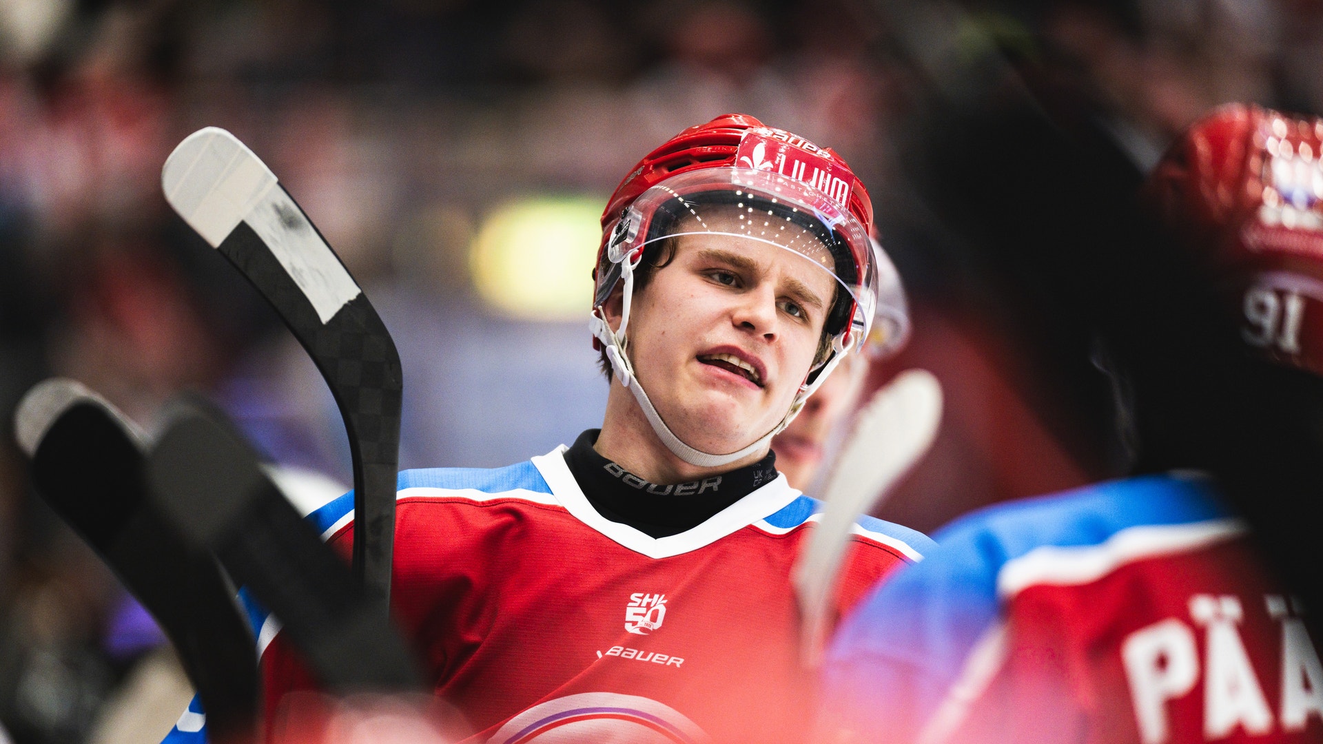 Ishockeyspelare i röd tröja och röd hjälm håller en ishockeyklubb under en match.