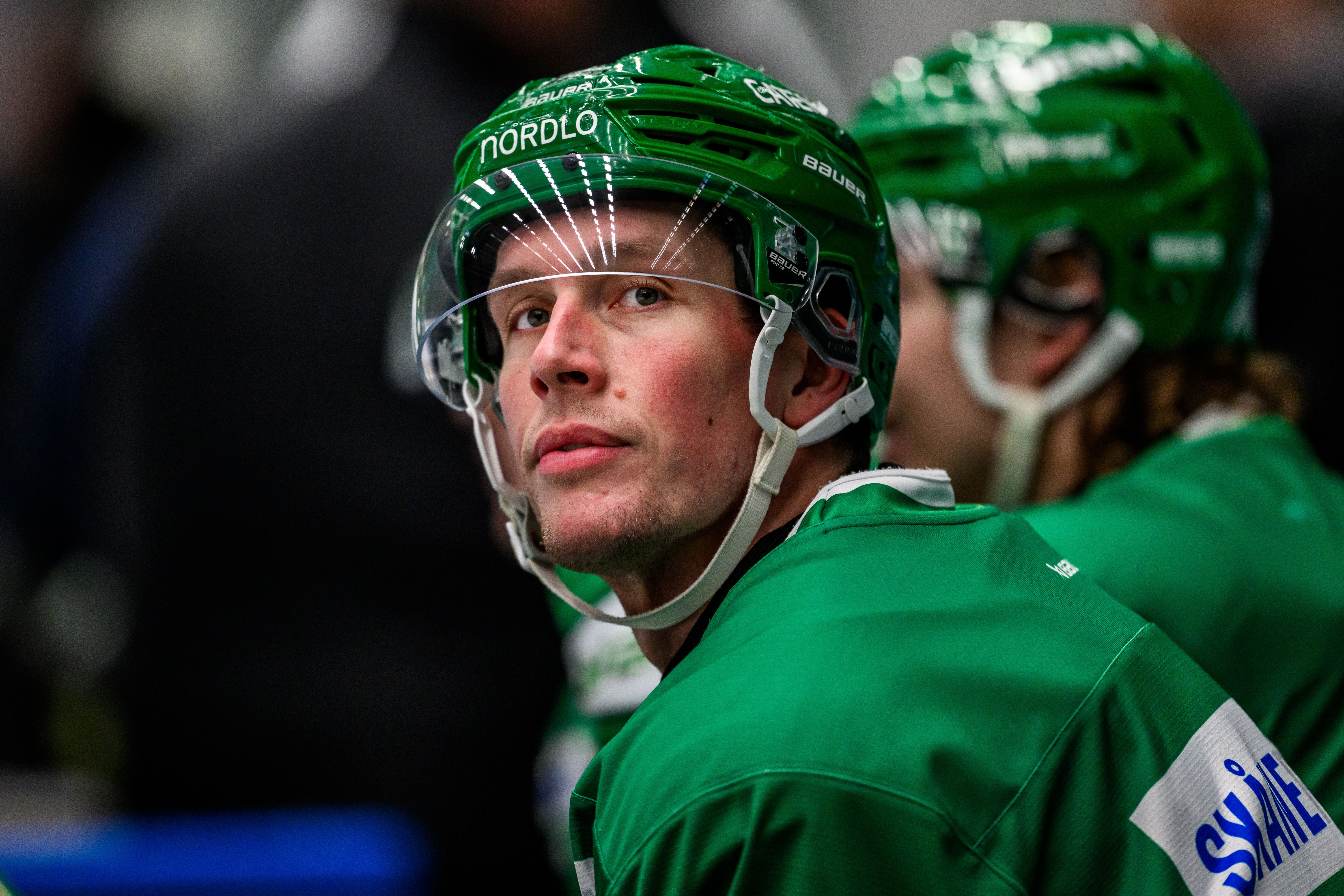 Ishockeyspelare i grönt och vitt lag klädd i matchutrustning och hjälm, fotograferad under en match på isen.