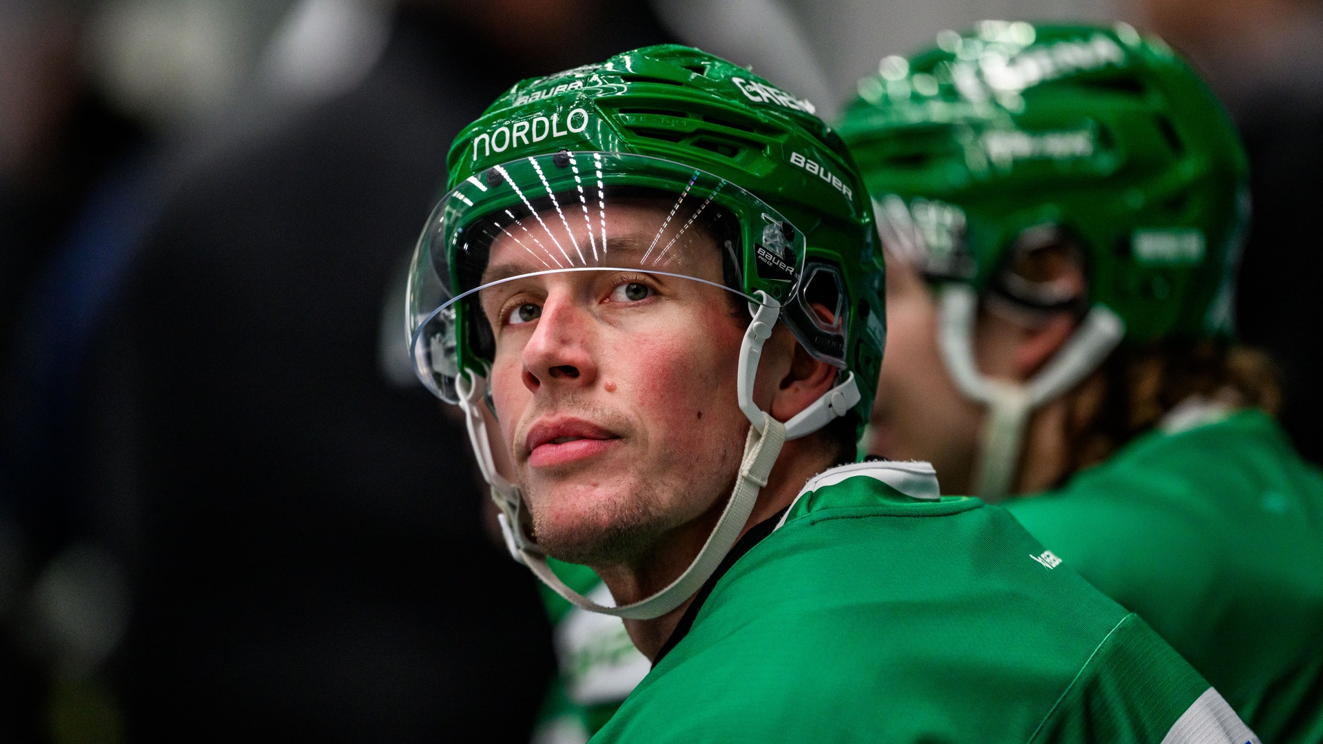 Ishockeyspelare i grönt och vitt lag klädd i matchutrustning och hjälm, fotograferad under en match på isen.