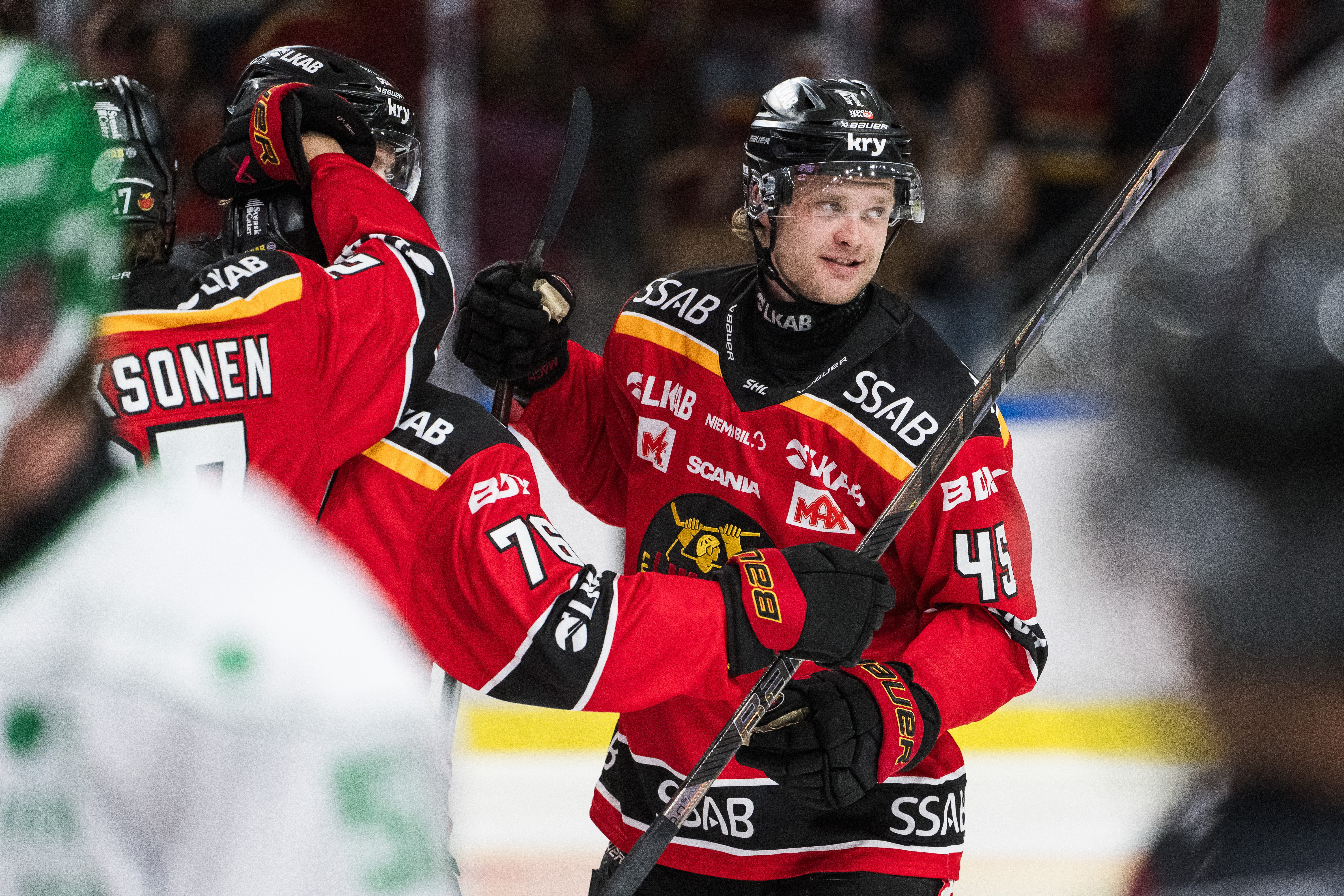 Ishockeyspelare i röd matchtröja jublar tillsammans med en lagkamrat på isen.