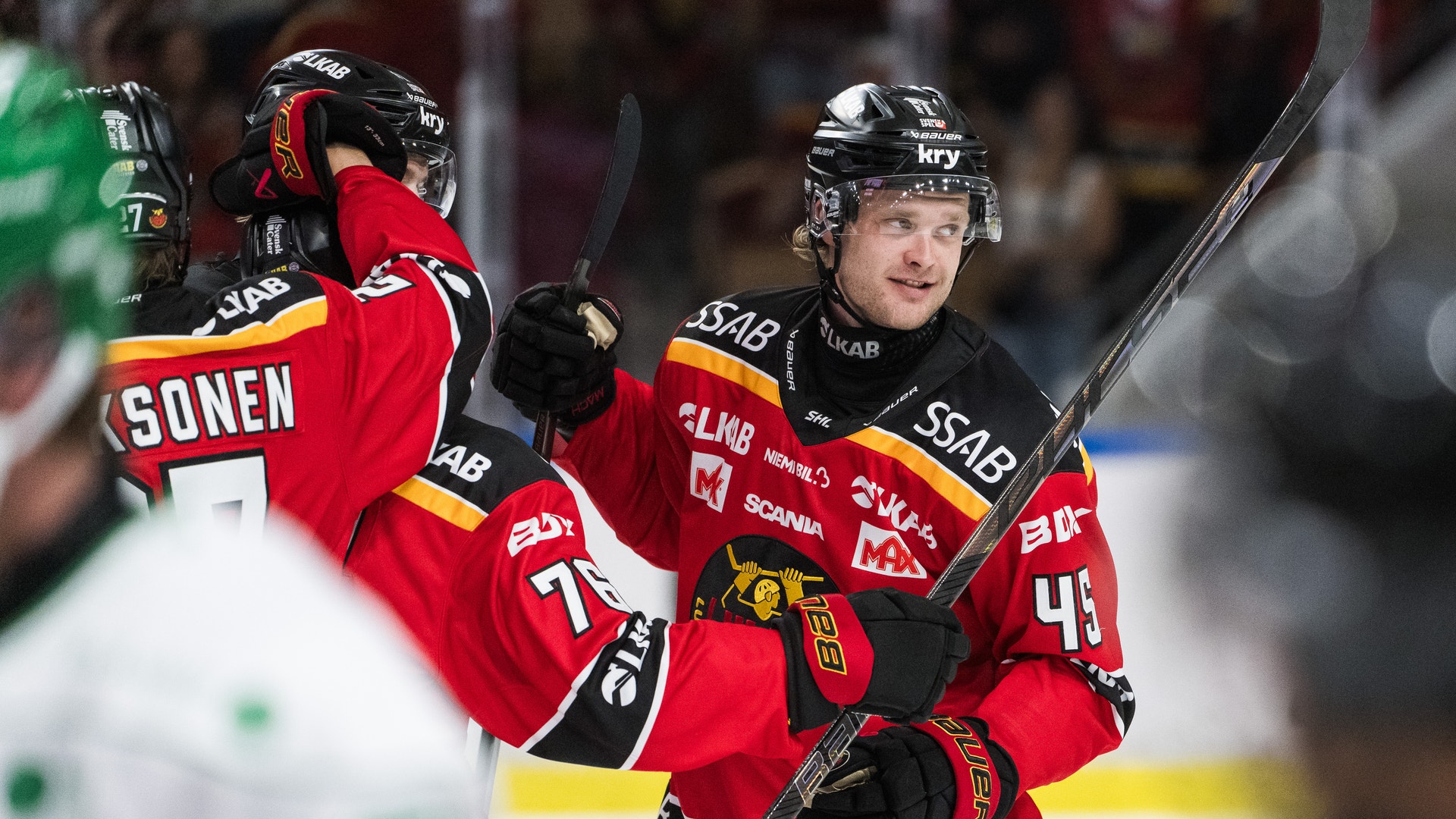 Ishockeyspelare i röd matchtröja jublar tillsammans med en lagkamrat på isen.