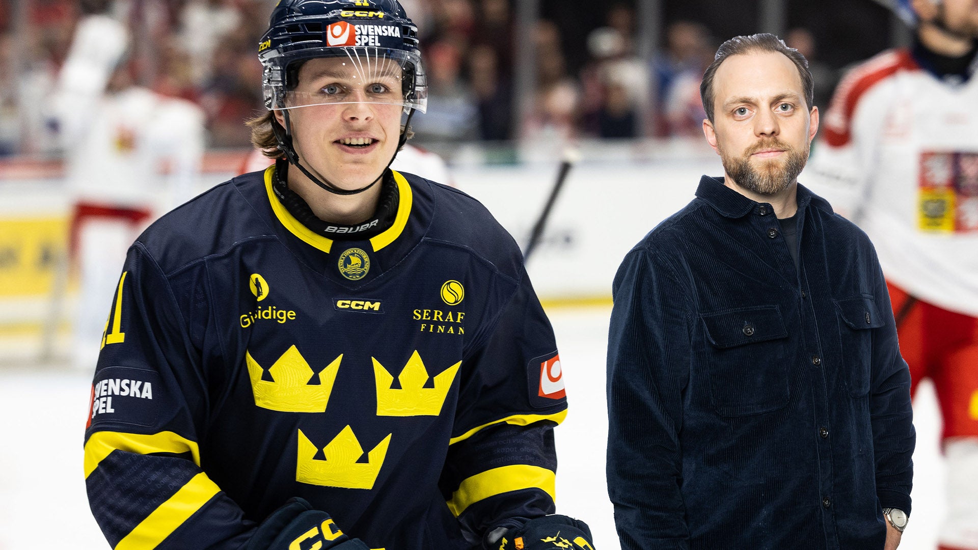 En ishockeyspelare i Sveriges landslags blå tröja med gula tre kronor står på isen tillsammans med en man i svart jacka.