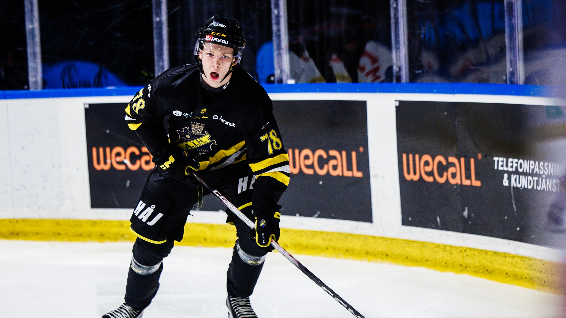Ishockeyspelare i svart och gul uniform spelar på isen med hockeyklubbe och puck under en match.