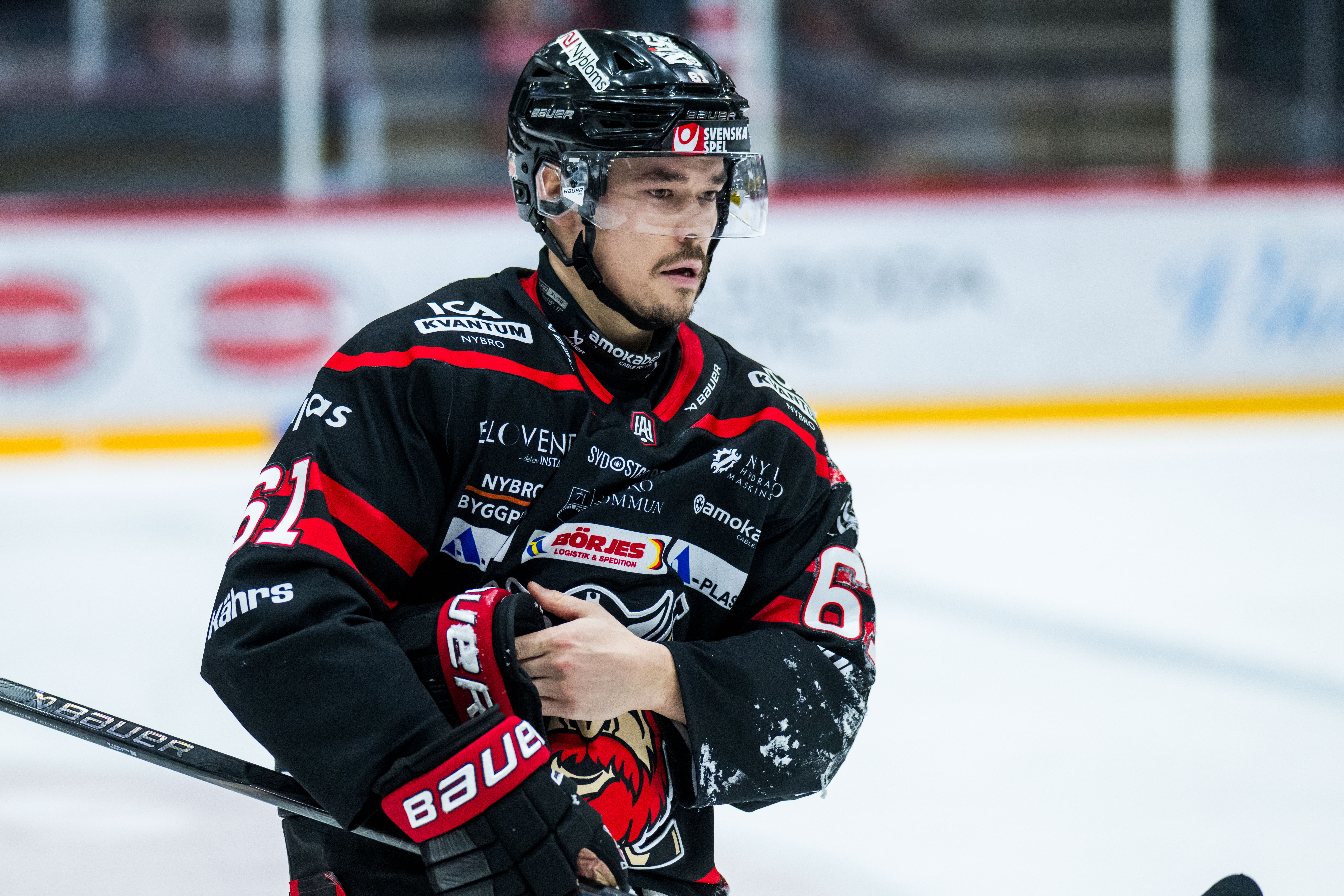 Ishockeyspelare i röd och svart uniform står på isen med sin hockeyklubb under ett match.