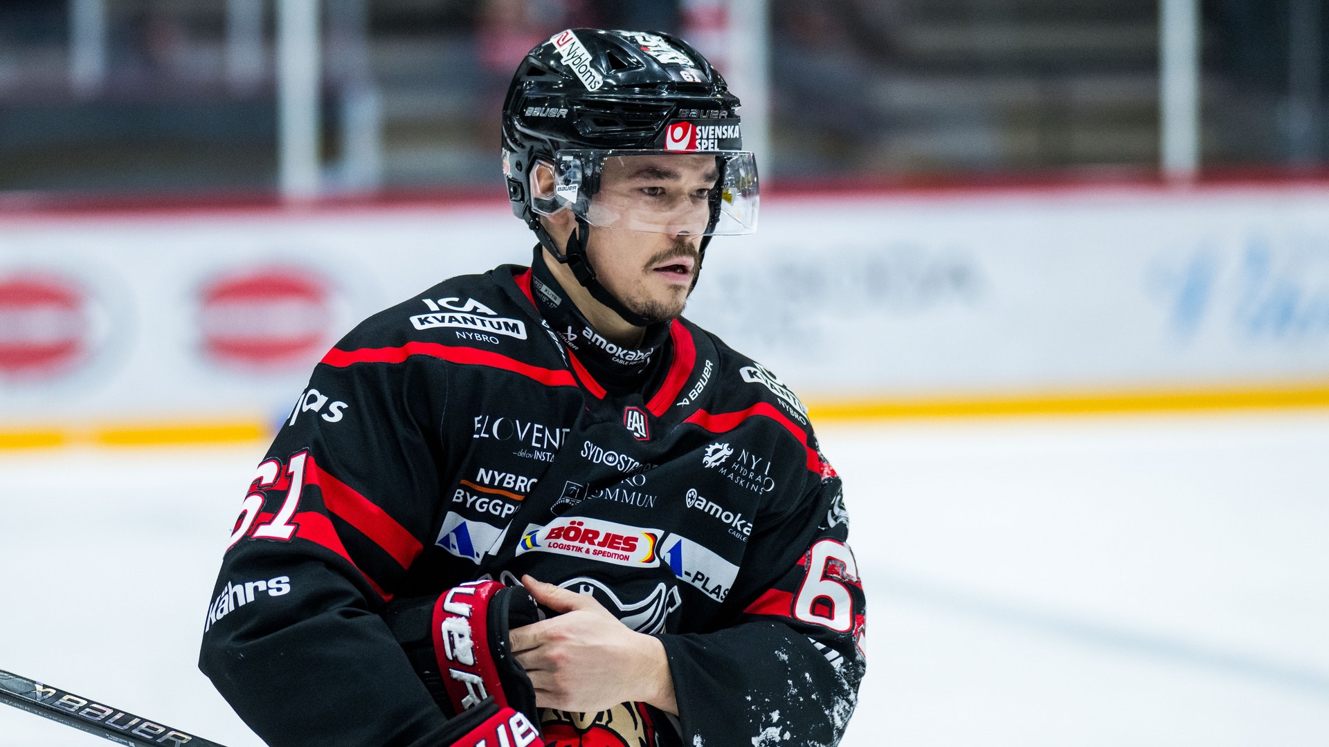 Ishockeyspelare i röd och svart uniform står på isen med sin hockeyklubb under ett match.
