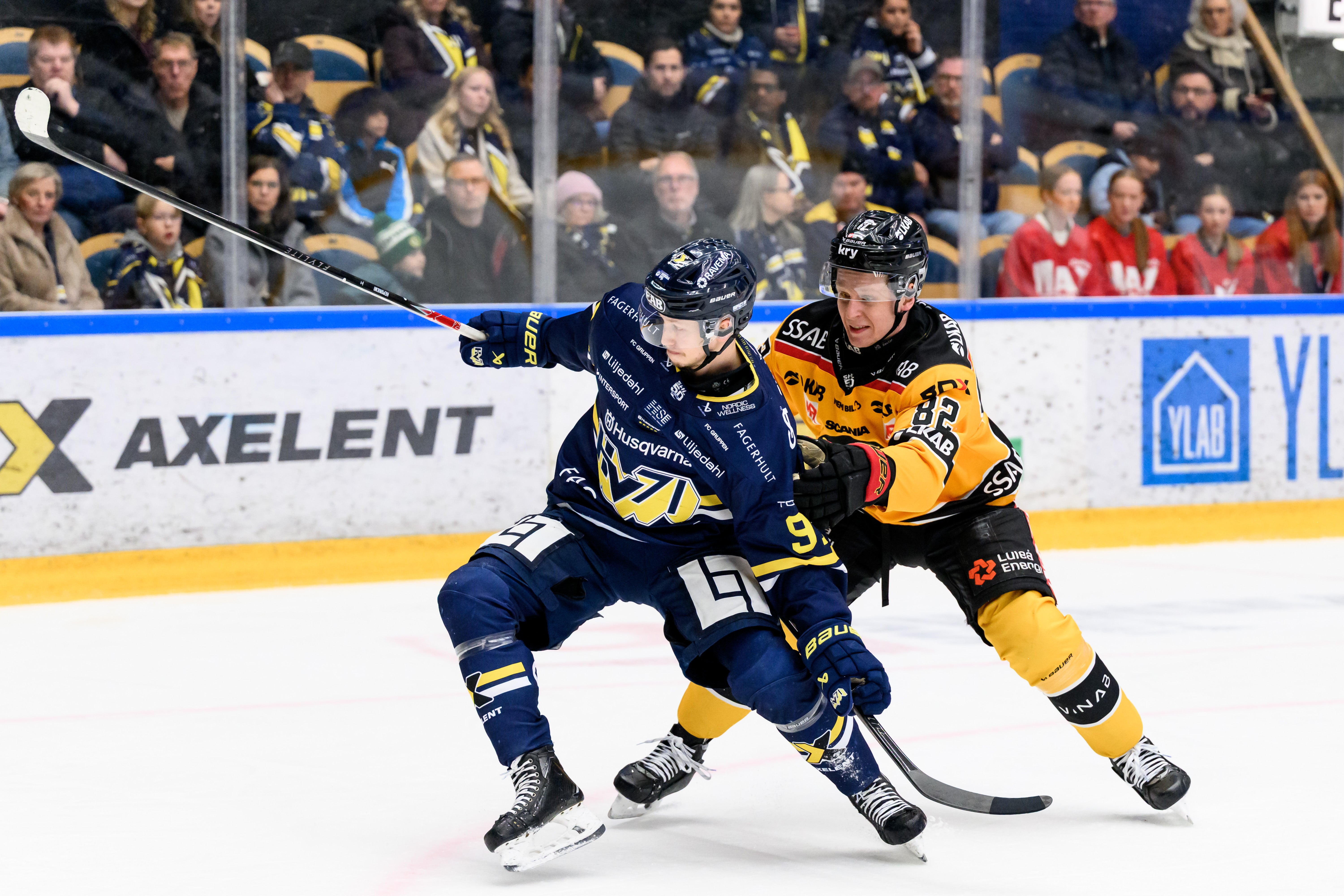 Ishockeymatch där en spelare i mörkblå och gul tröja kontrollerar pucken på isen under en match.