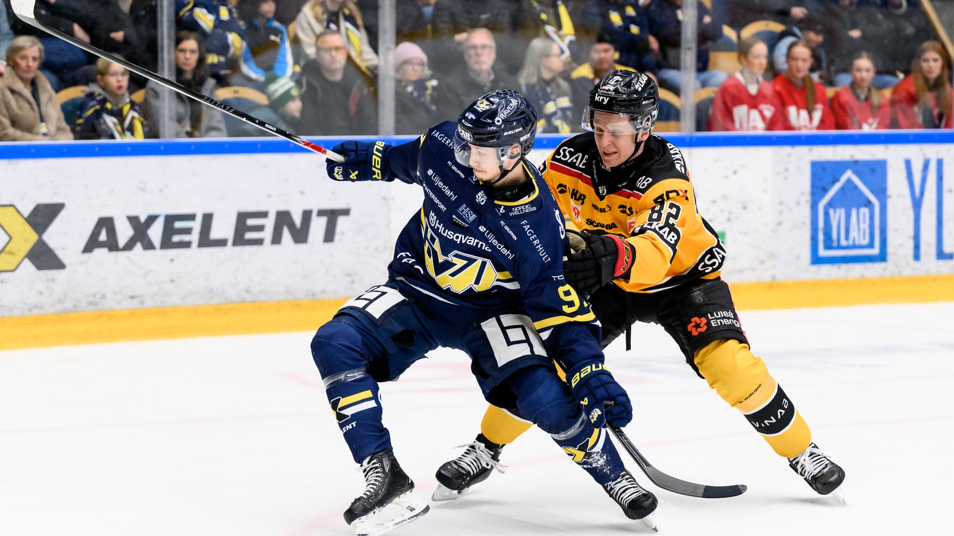 Ishockeymatch där en spelare i mörkblå och gul tröja kontrollerar pucken på isen under en match.