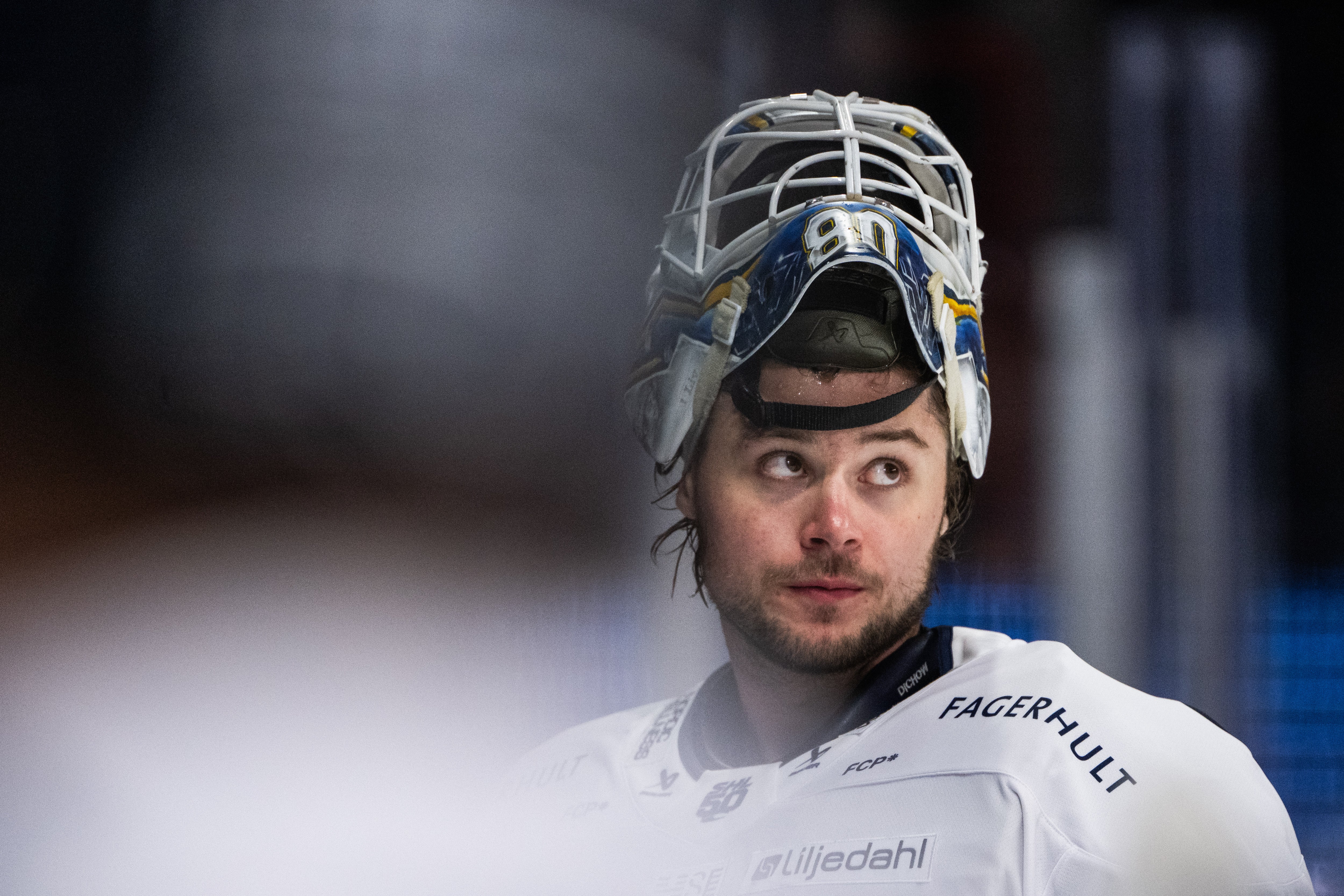 Porträtt av en ishockeyspelare i målvaktsuniform med vit utrustning och målvaktsmask.