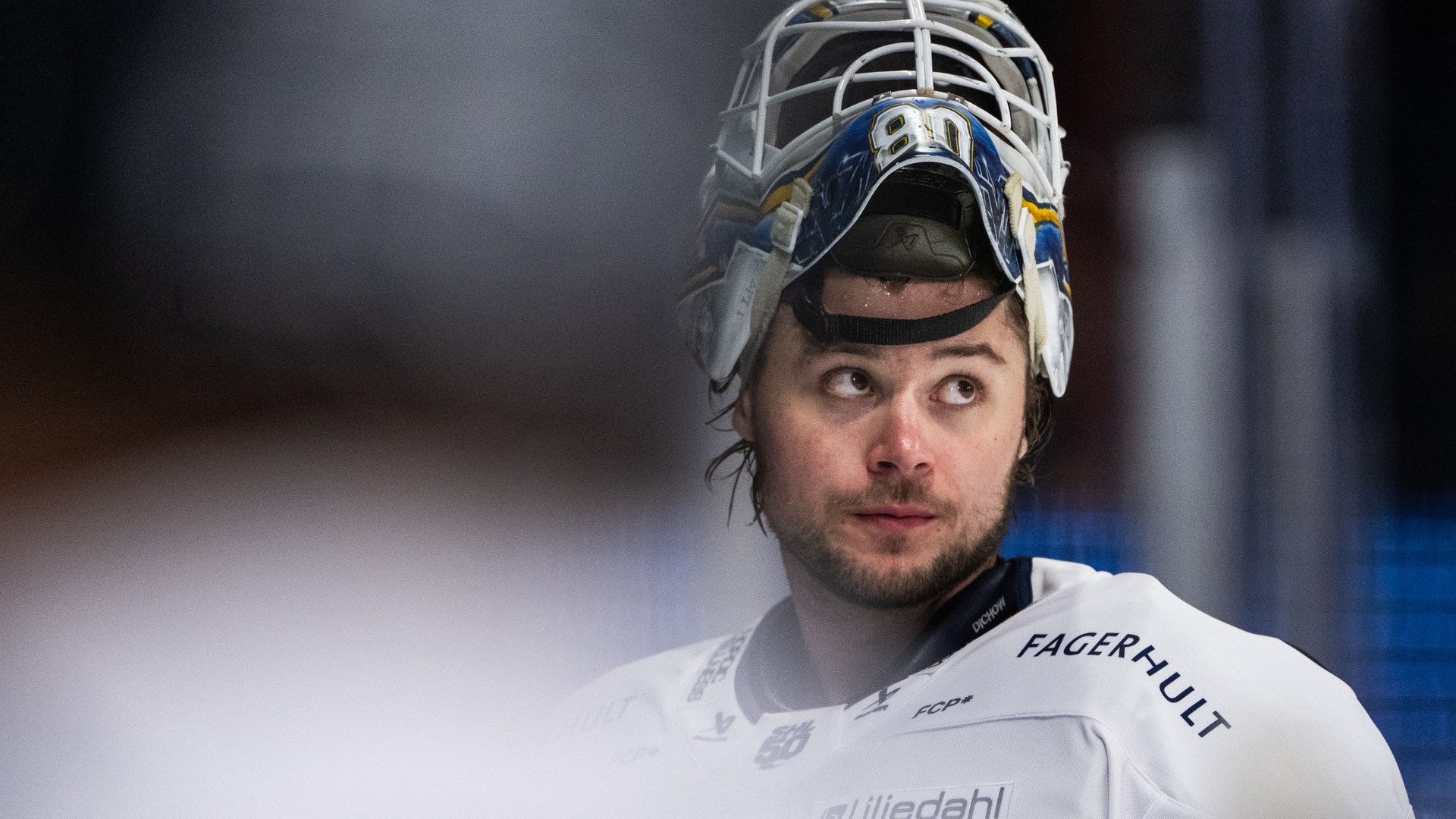 Porträtt av en ishockeyspelare i målvaktsuniform med vit utrustning och målvaktsmask.