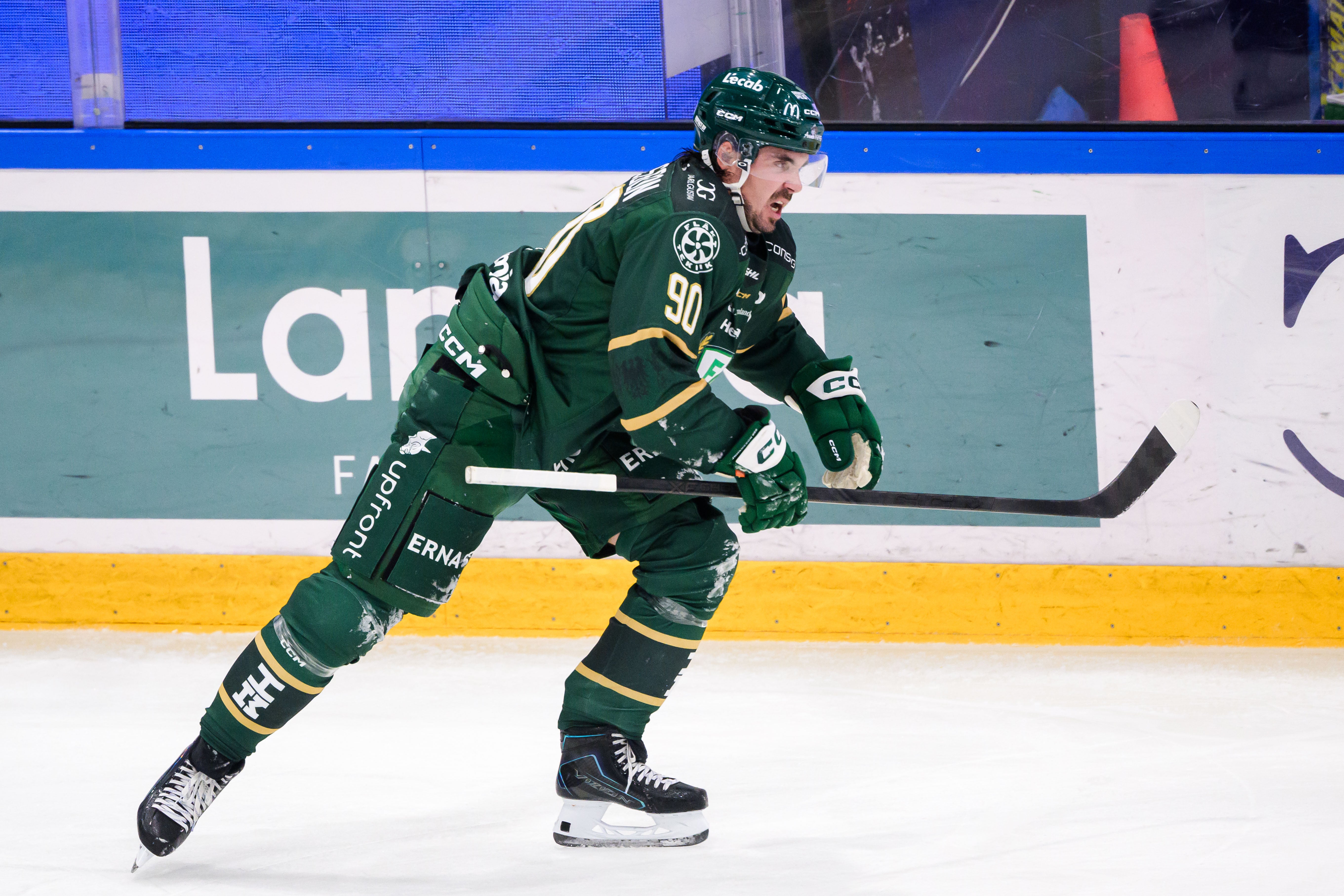 En ishockeyspelare i grön matchtröja skridskoåker och sträcker fram klubban på isen.