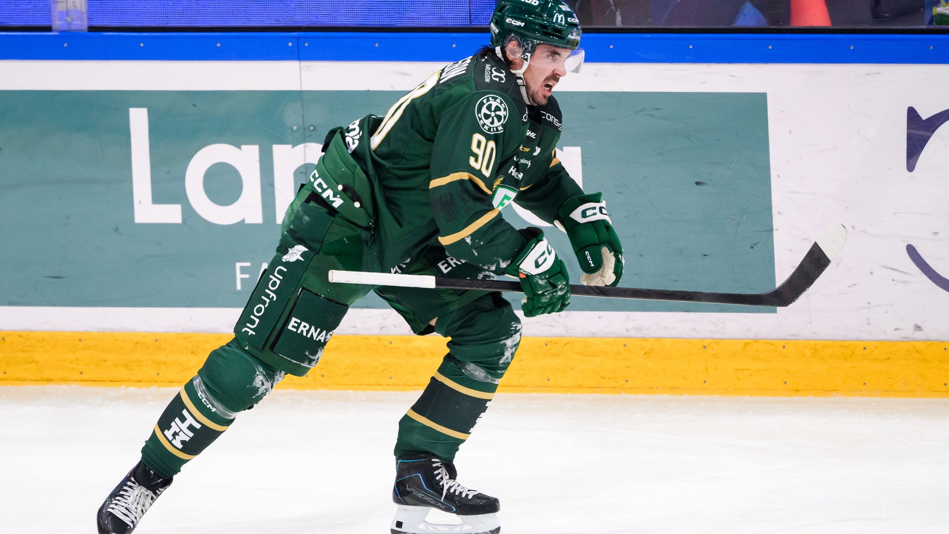 En ishockeyspelare i grön matchtröja skridskoåker och sträcker fram klubban på isen.