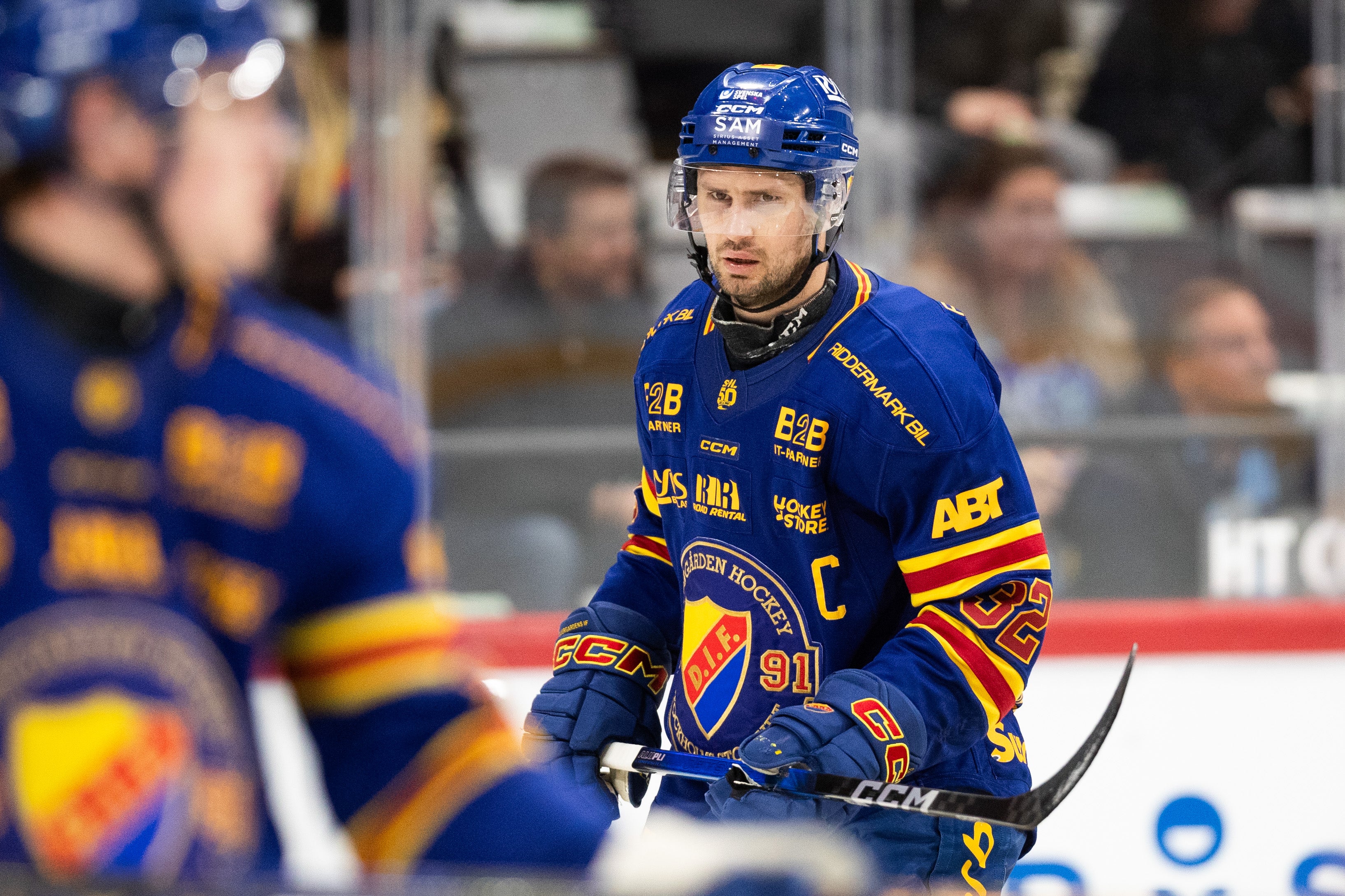 Ishockeyspelare i blå och gul tröja med C-märke på isen under en match.
