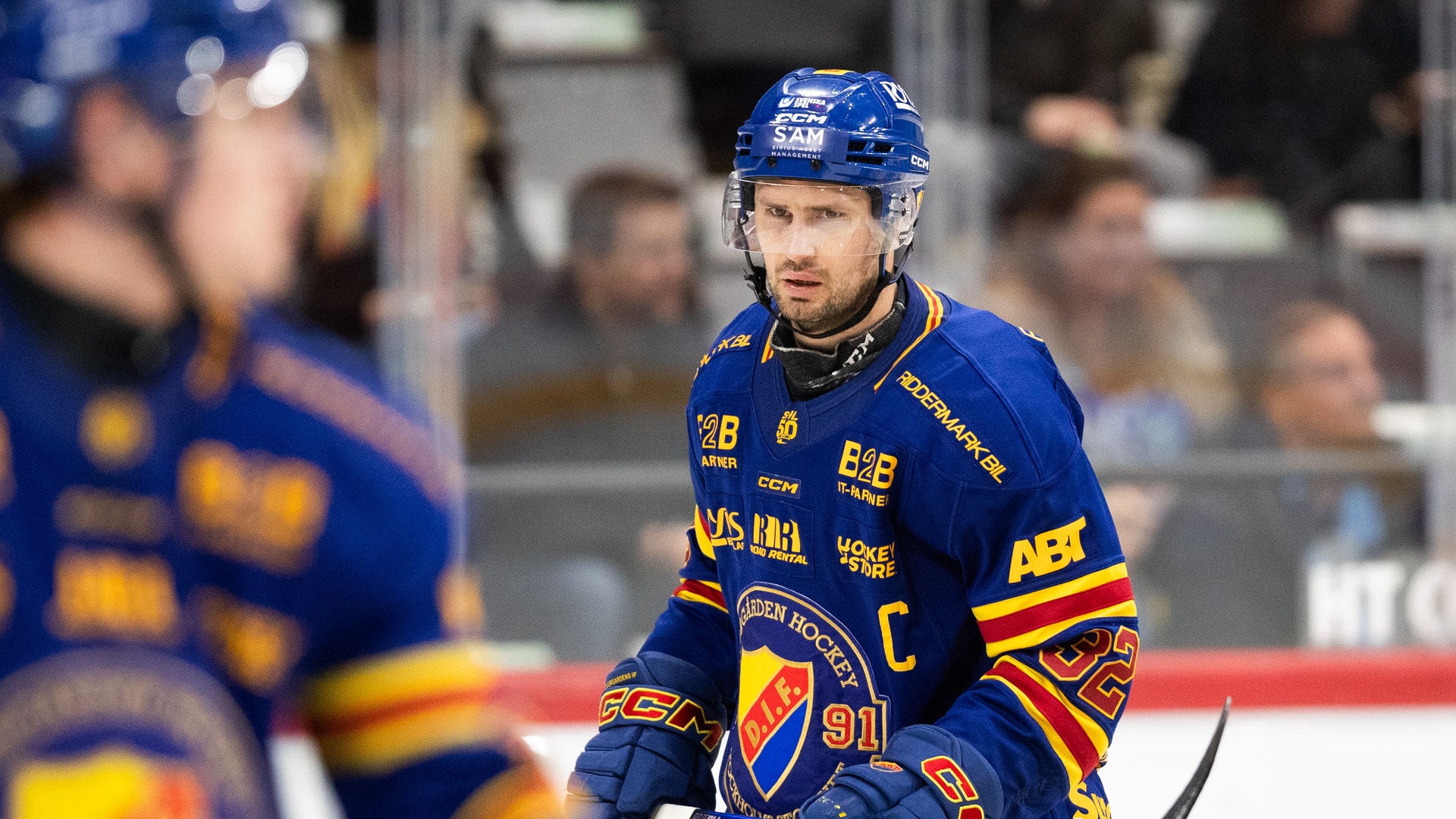 Ishockeyspelare i blå och gul tröja med C-märke på isen under en match.