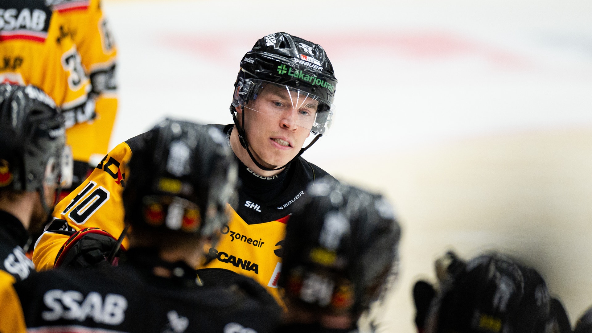 Ishockeyspelare i gul och svart uniform med hjälm under en match.