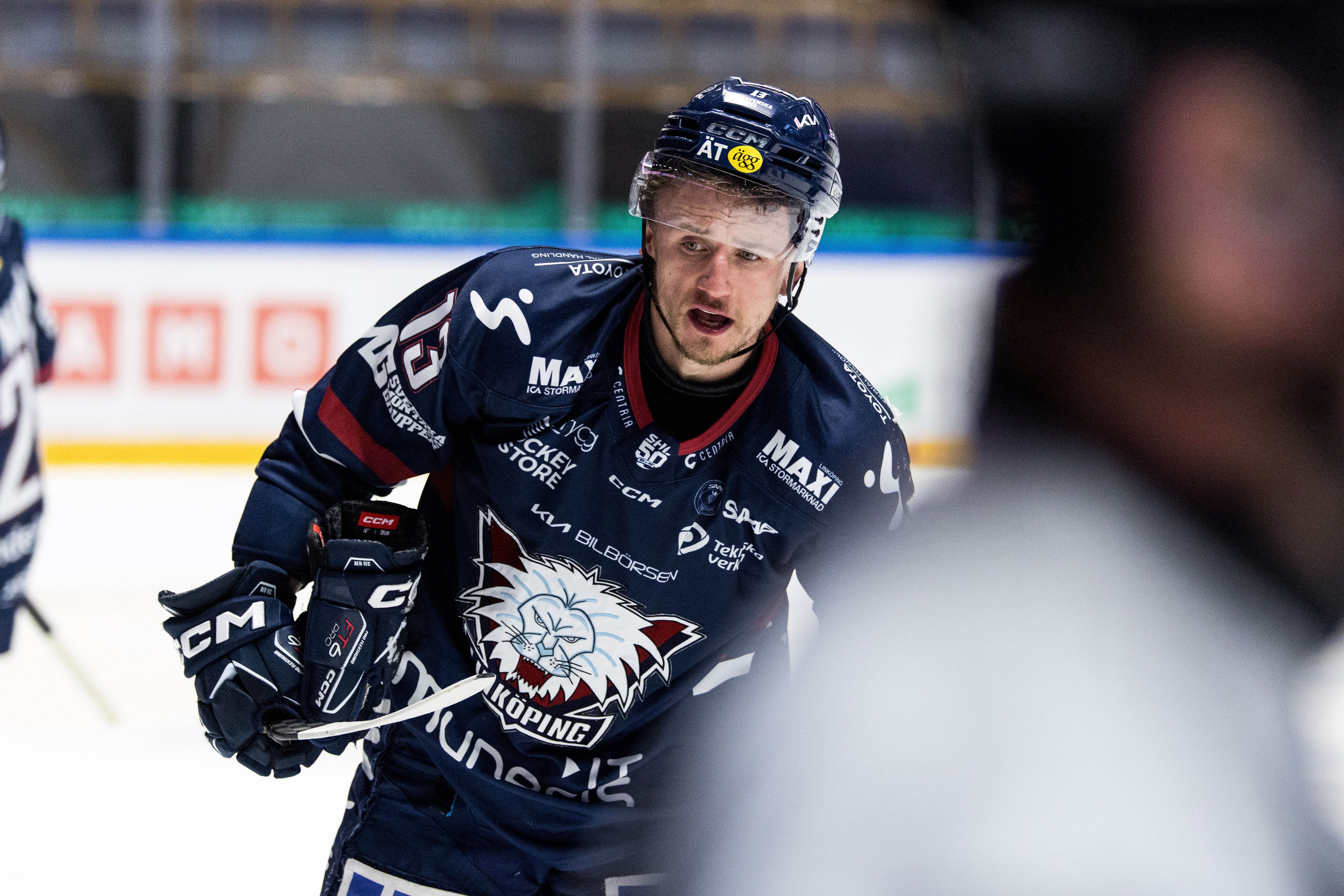 Ishockeyspelare i mörkblå tröja med hjälm spelar under en match på isen.