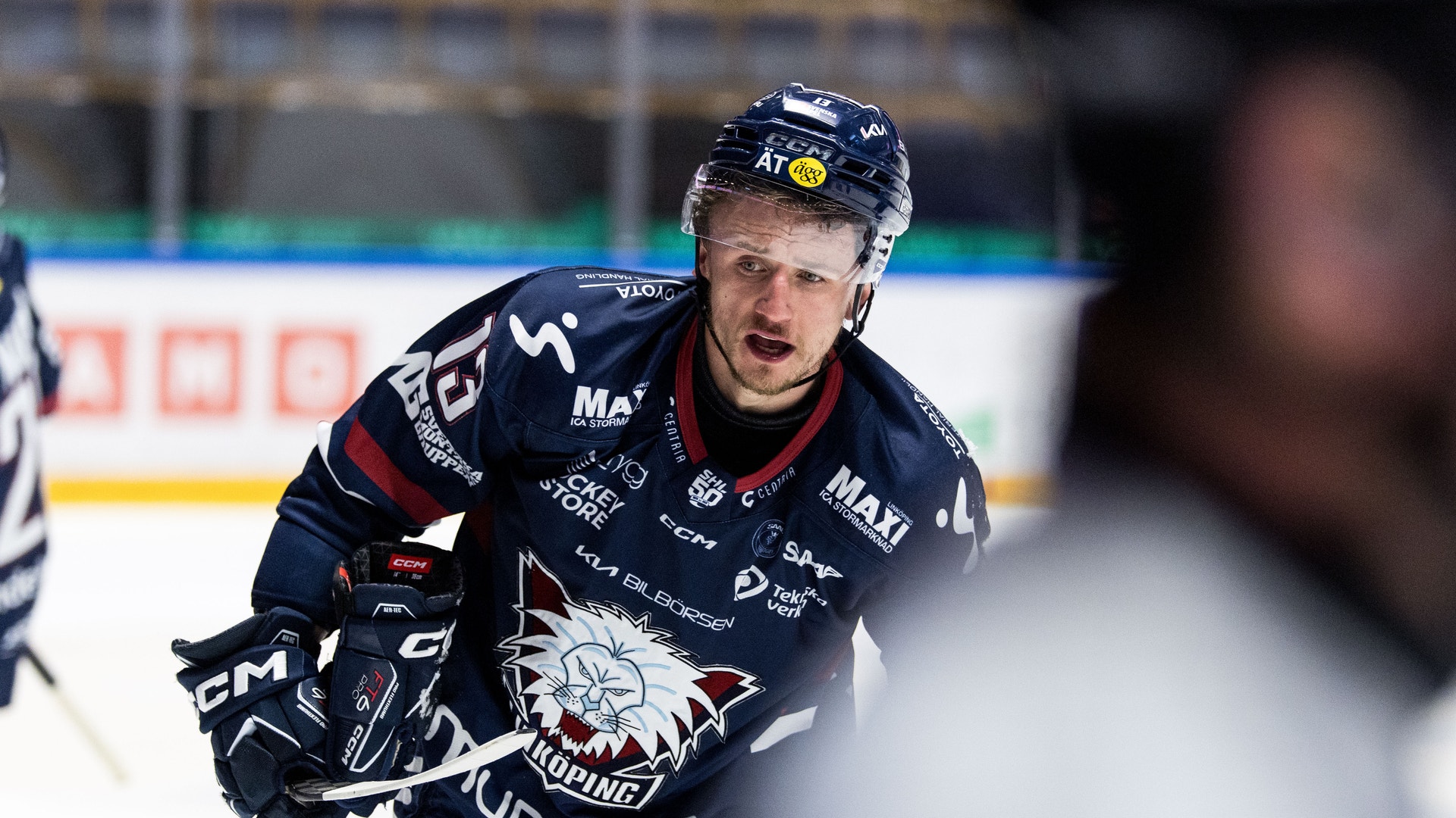 Ishockeyspelare i mörkblå tröja med hjälm spelar under en match på isen.